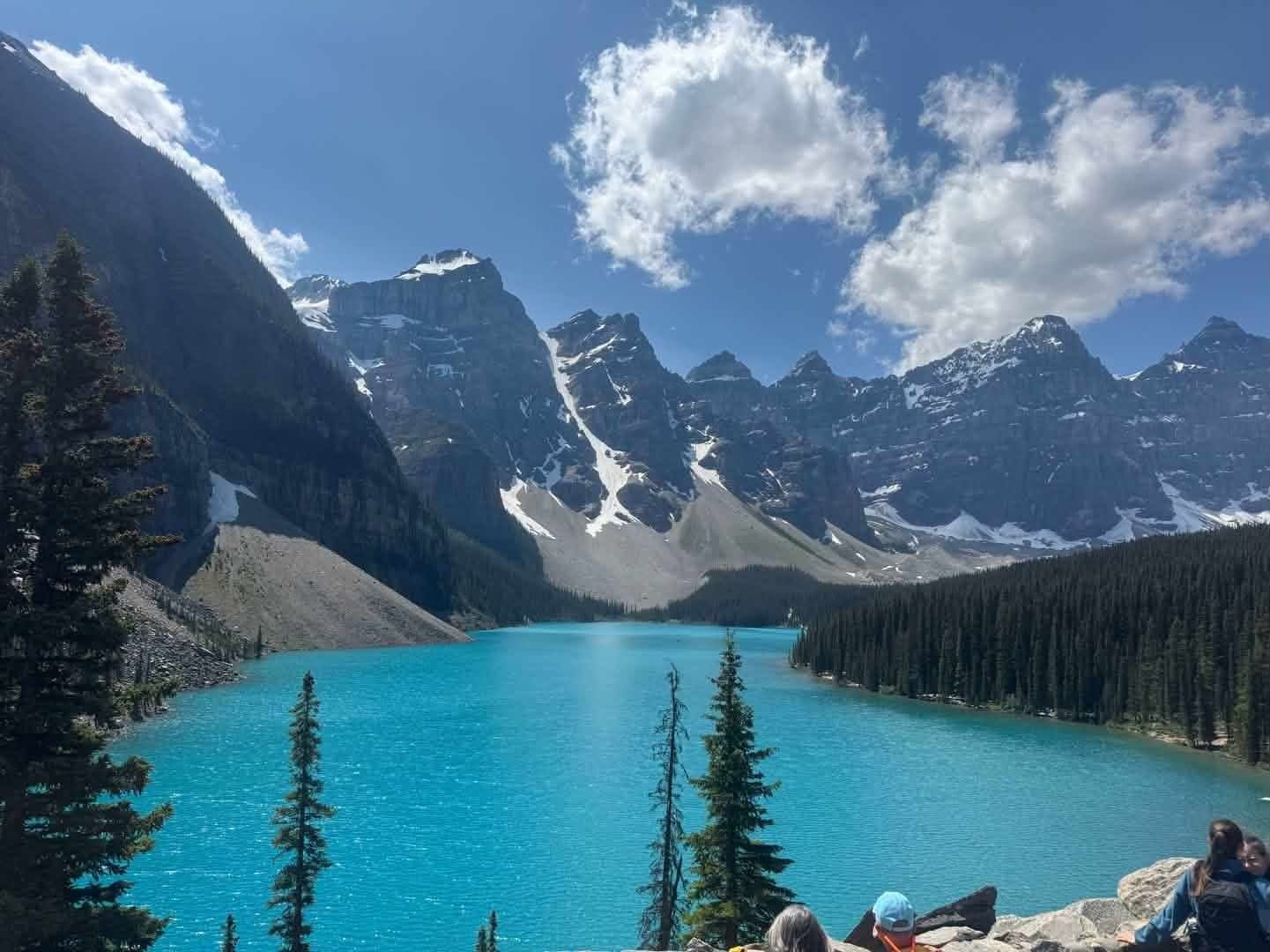 Turquoise alpine lake with snowy mountain peaks and pine trees under a partly cloudy sky