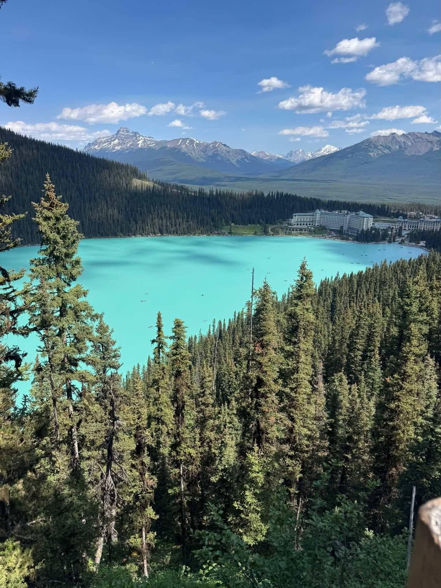 Turquoise mountain lake surrounded by pine forest with snowy peaks and a blue sky