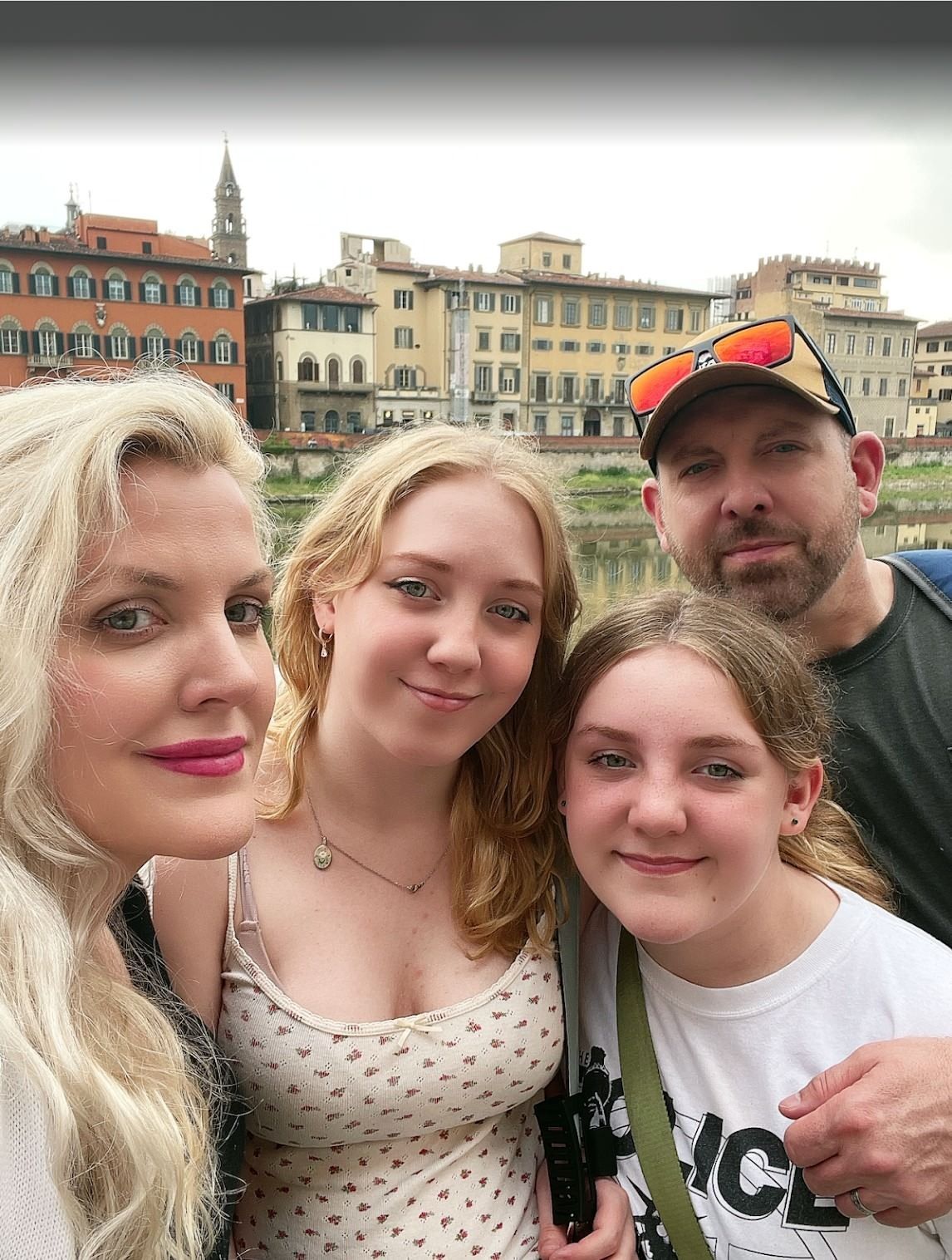 Four people posing for a selfie in front of colorful riverside buildings under a cloudy sky.