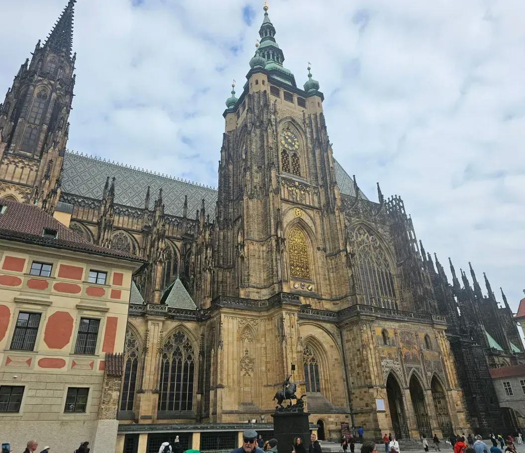 Gothic cathedral with twin spires and ornate stone facade in a city square under a cloudy sky