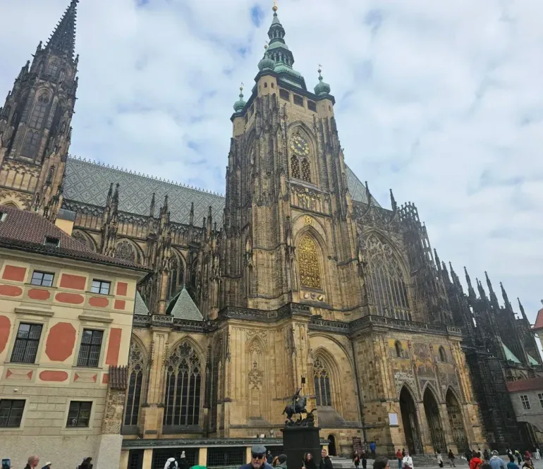 Gothic cathedral with twin spires and ornate stone facade in a city square under a cloudy sky