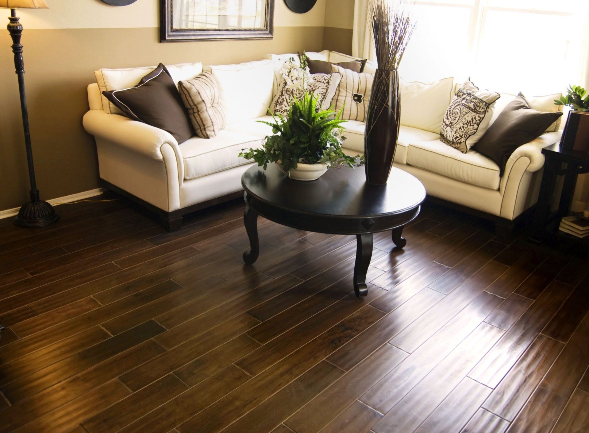 A cozy living room with a white sectional sofa, dark wooden coffee table, floor lamp, and polished dark wood floors.