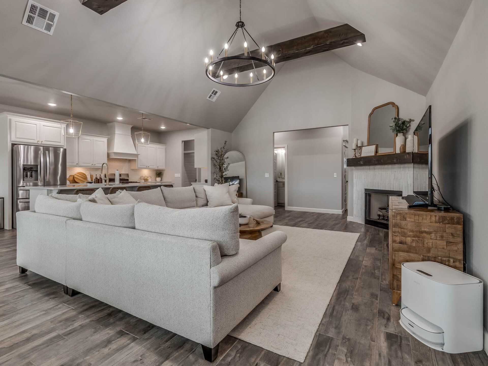 A modern open-plan living room with a white sectional sofa, vaulted ceilings, wooden beams, and an adjacent kitchen.