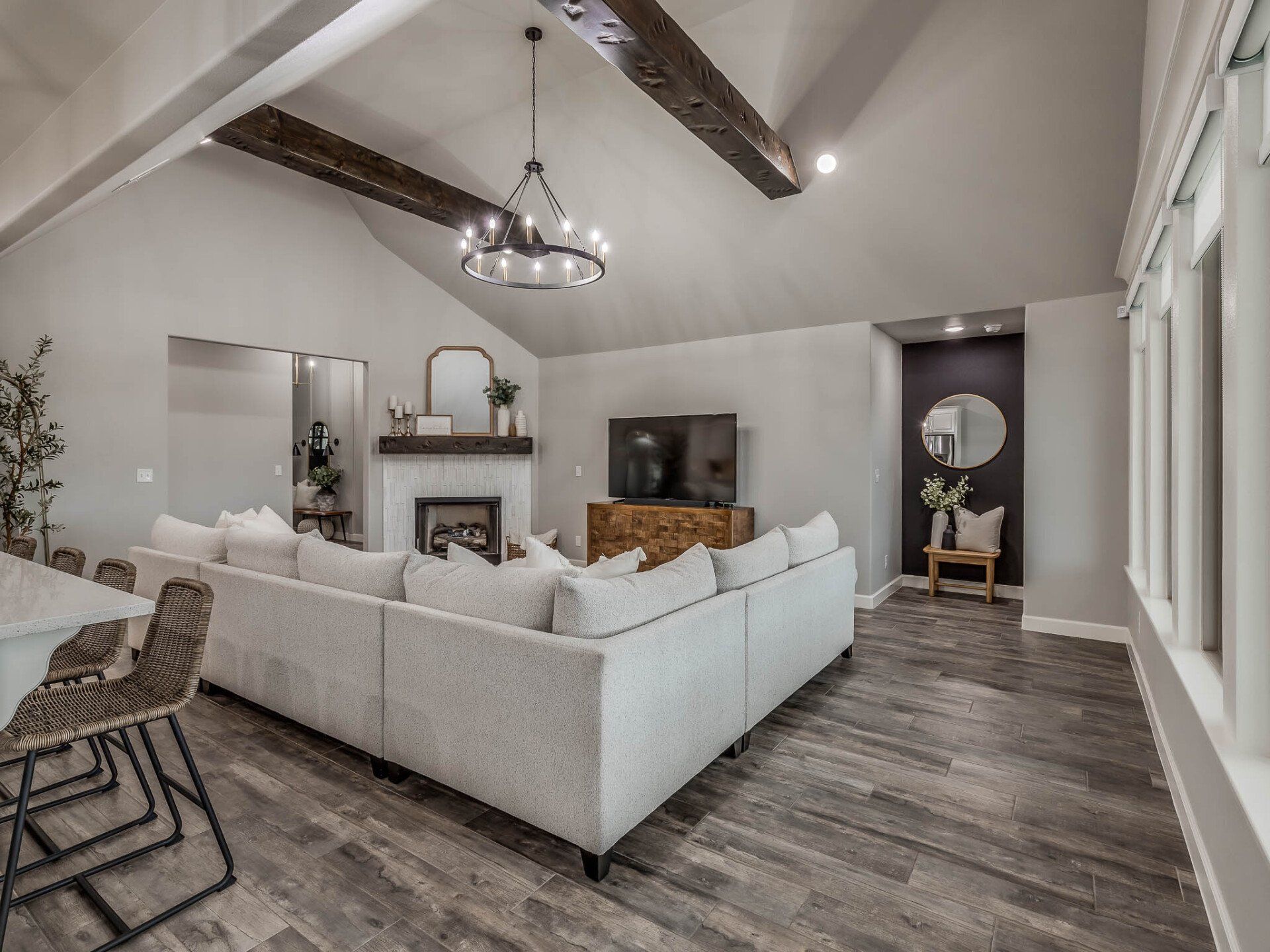 Modern living room with a large gray sectional, fireplace, television, wooden beams, and gray wood-look flooring.