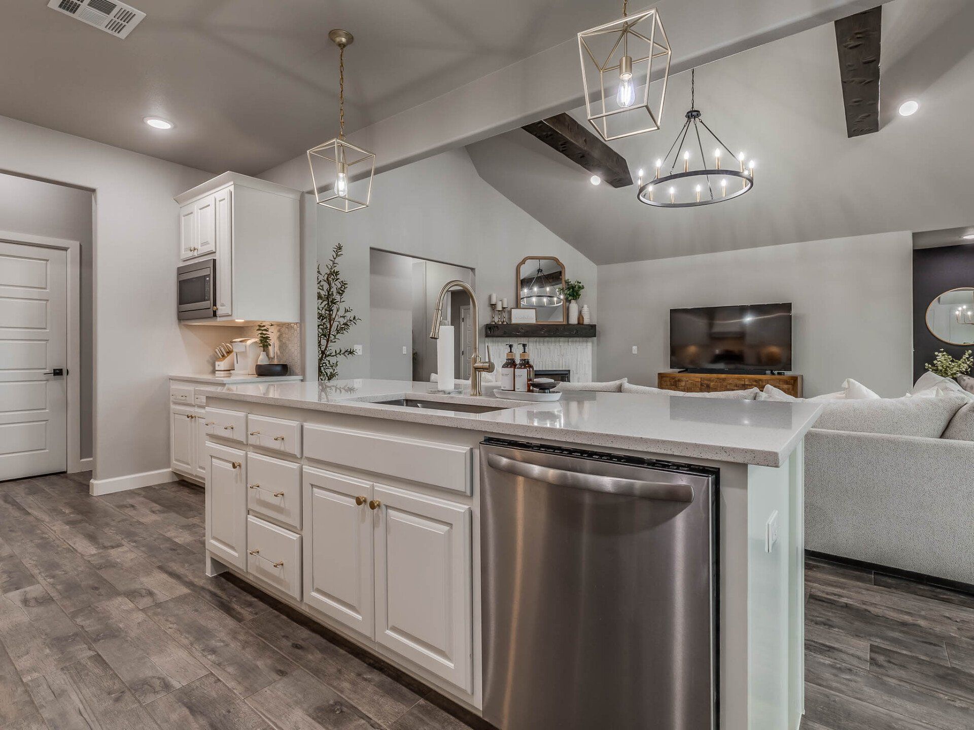 A kitchen island with a stainless-steel dishwasher, facing a bright, open-concept living area with wood-look tile floors.