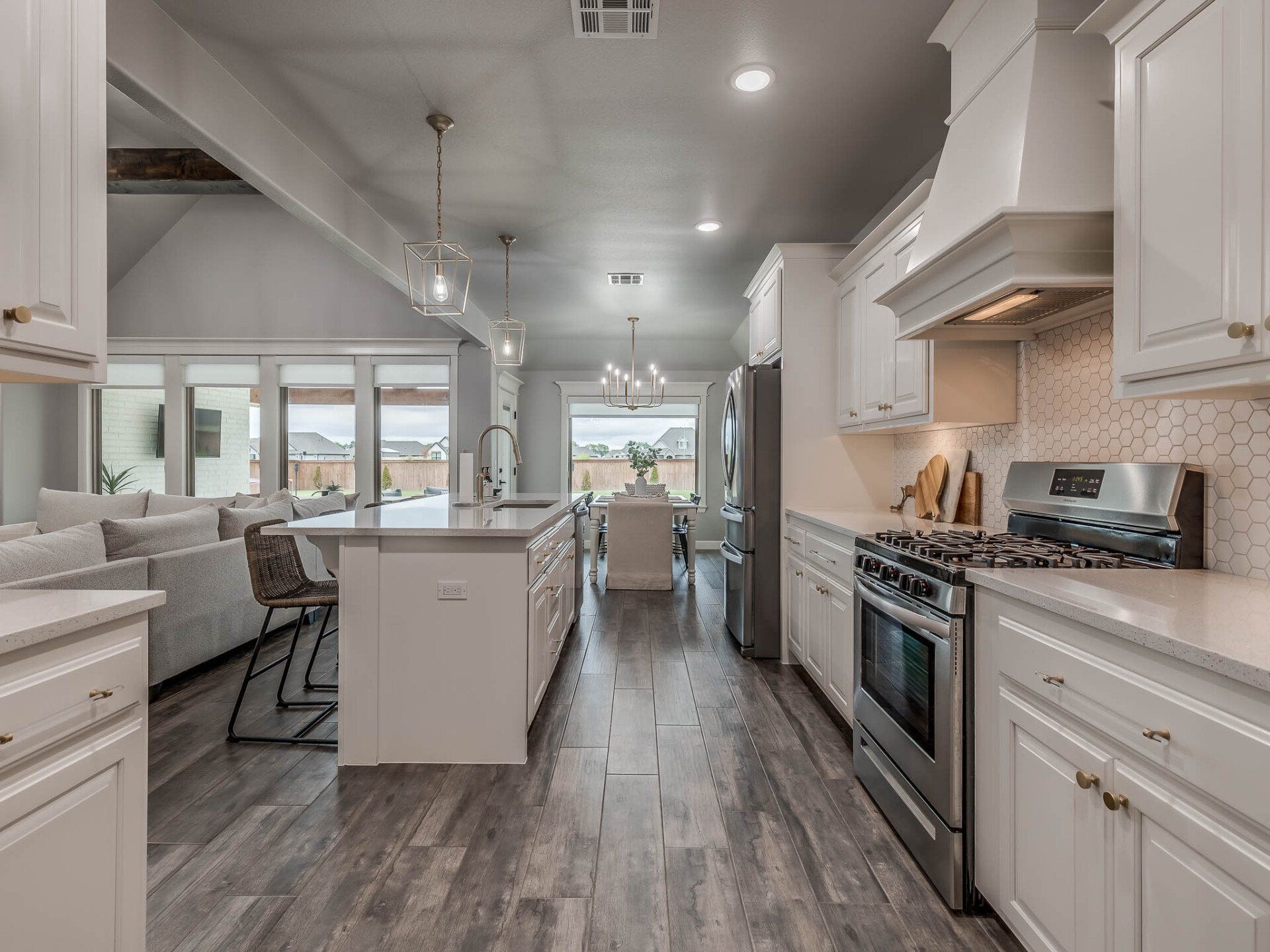 Modern kitchen with white cabinets, stainless steel appliances, a center island with stools, and grey wood-look flooring.