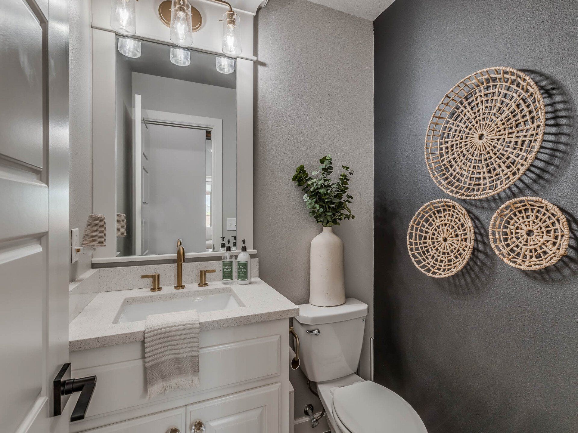 A small bathroom featuring white vanity, a grey textured wall decorated with three round woven baskets, and a toilet.
