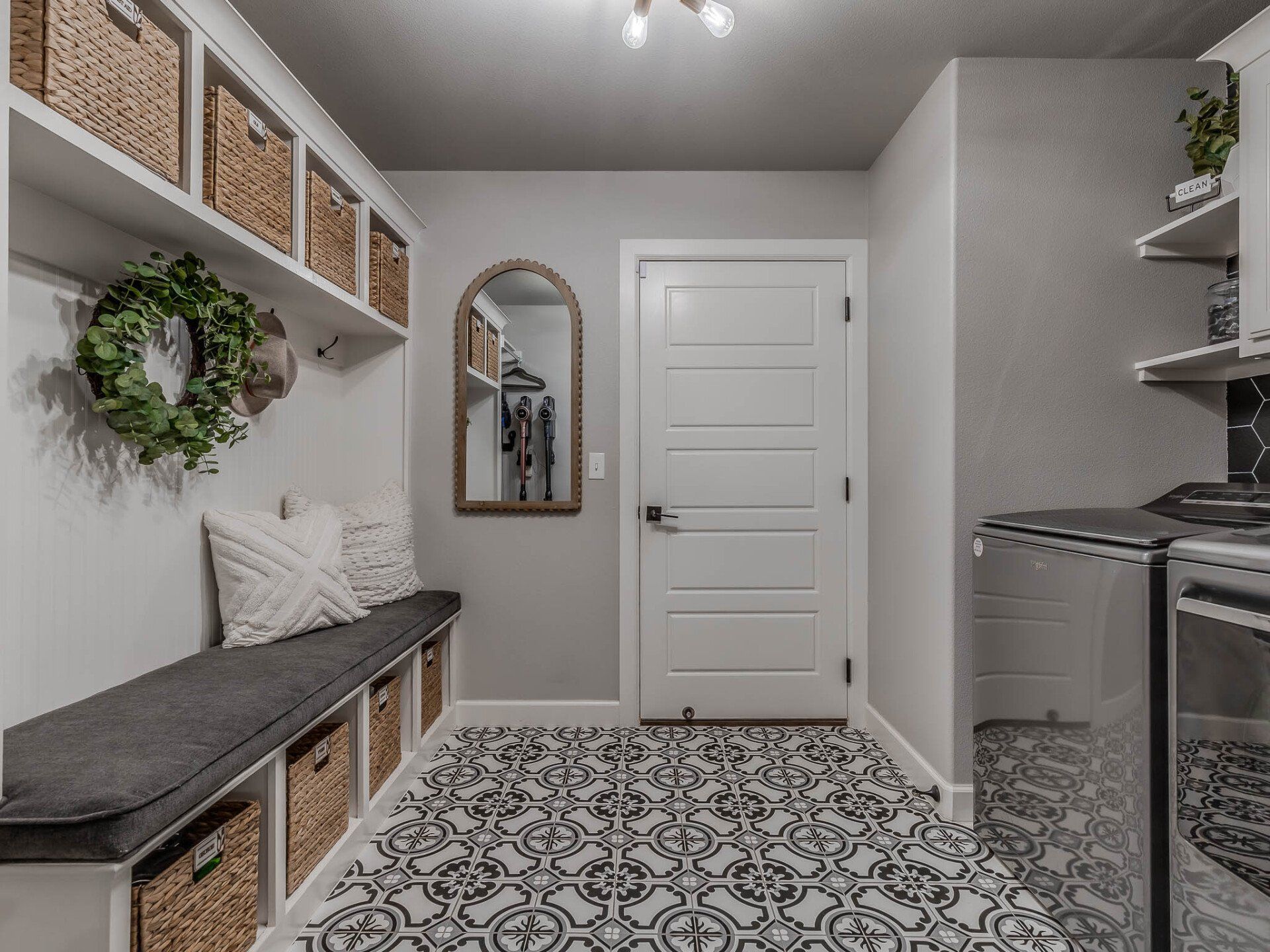 A mudroom featuring a built-in bench with wicker storage baskets, a decorative wreath, and patterned floor tiles.