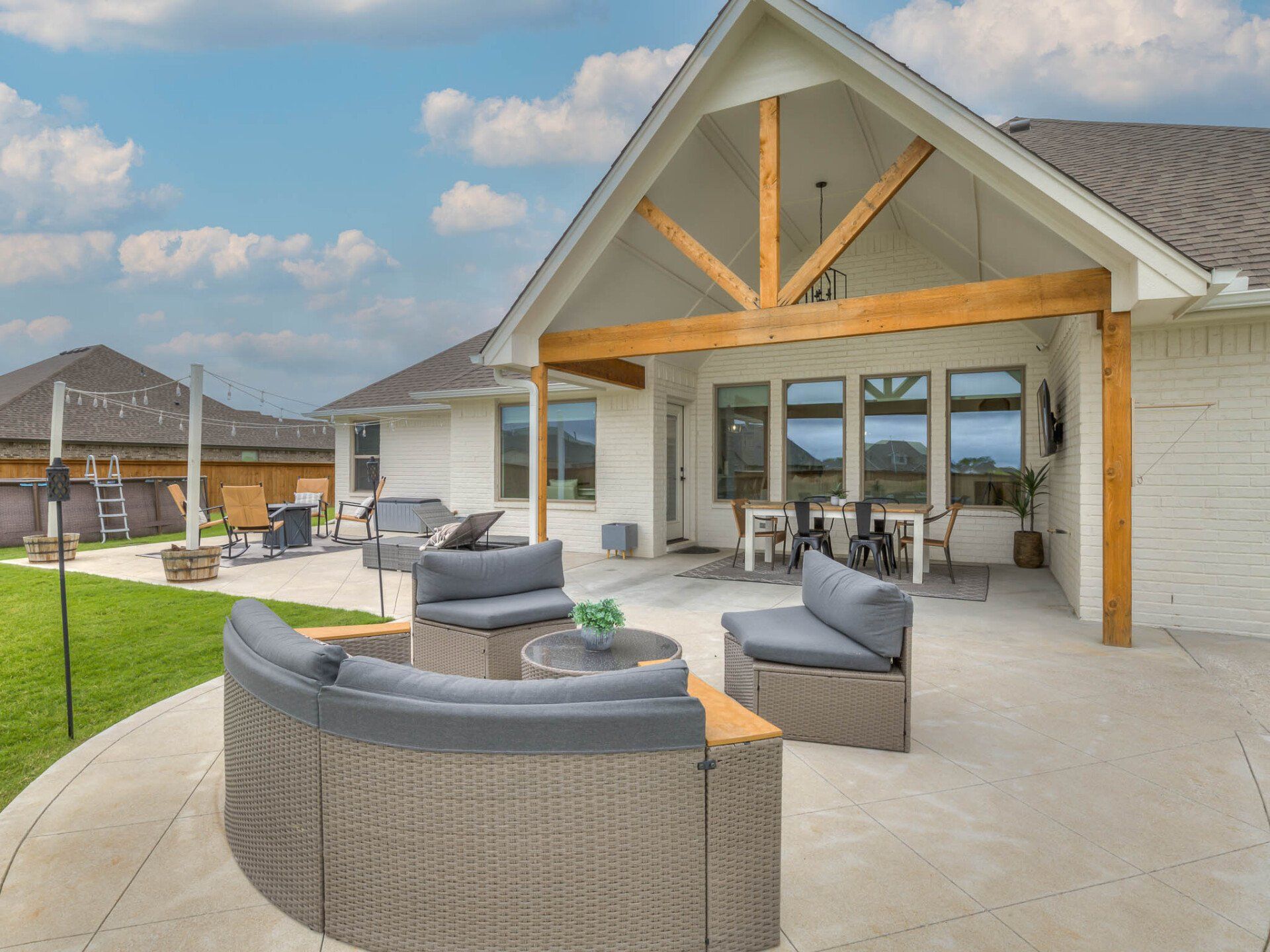 A patio with curved grey wicker sectional seating and a covered outdoor dining area under a wooden vaulted porch roof.