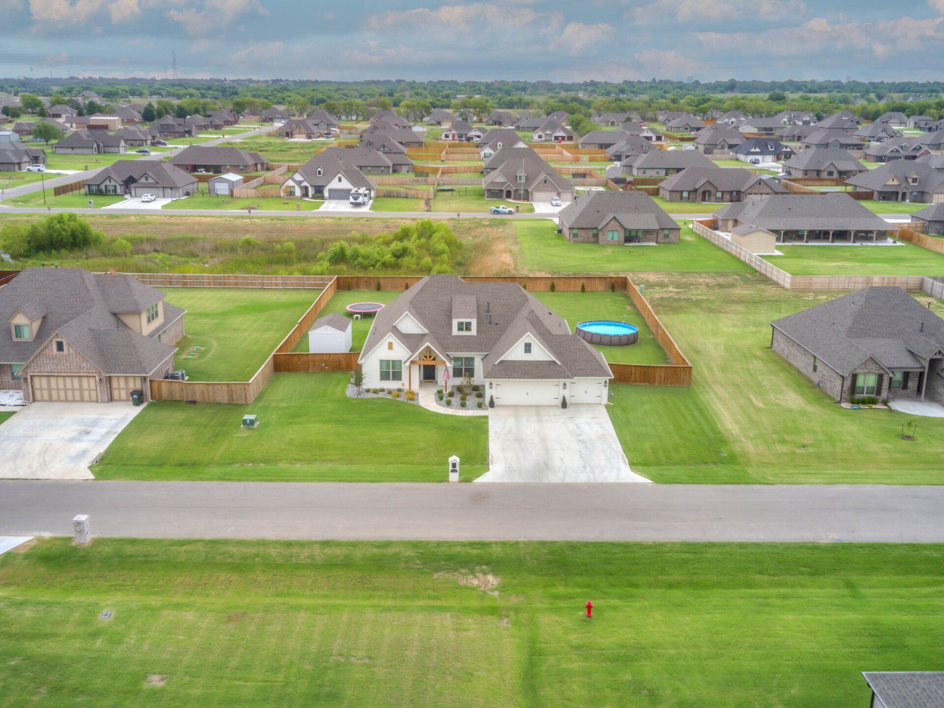 Aerial view of a residential suburban neighborhood featuring a central house with a white exterior and brown roof.