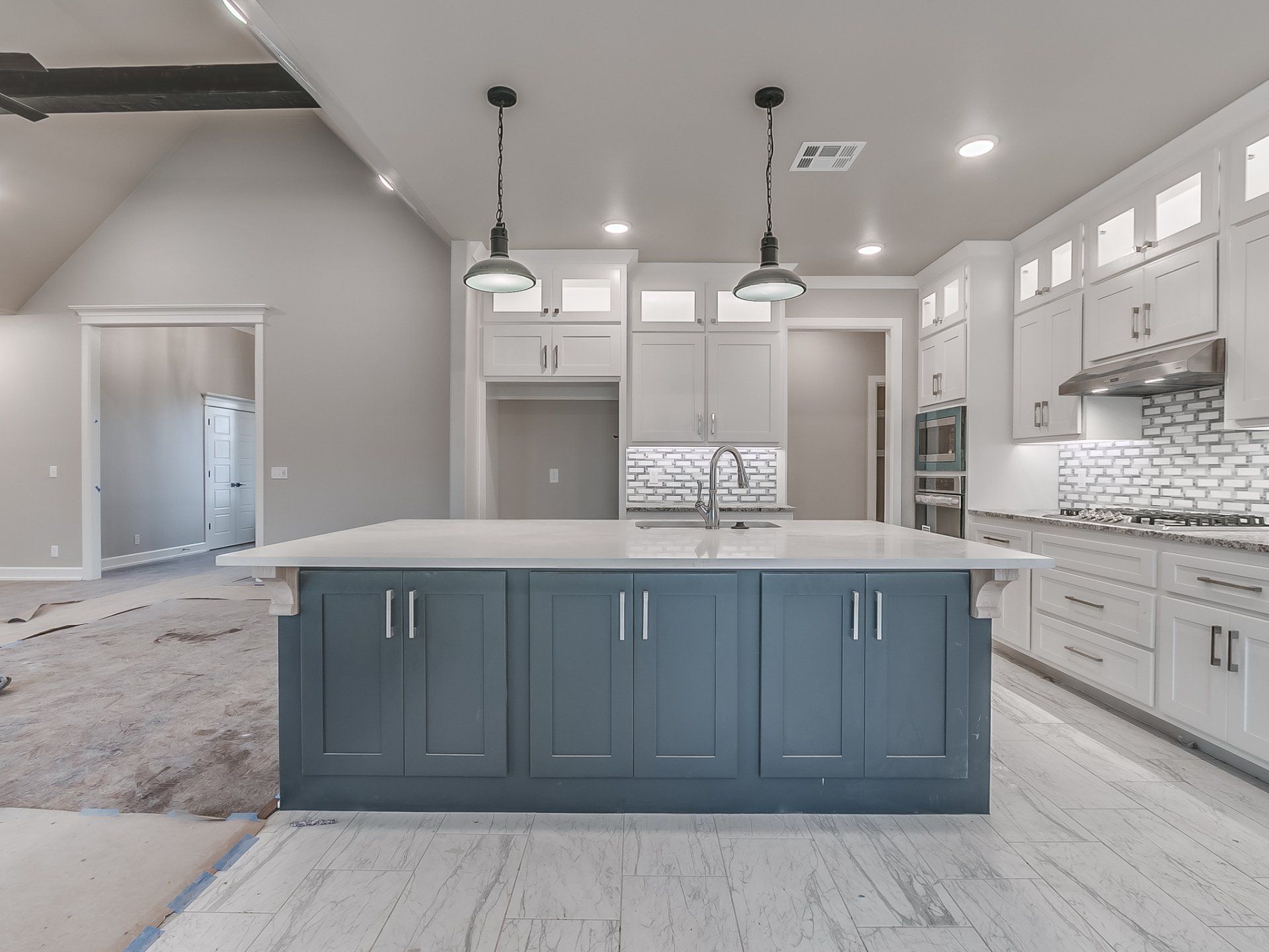 A modern kitchen with a large, dark blue island, white cabinets, tiled backsplash, and pendant lighting.
