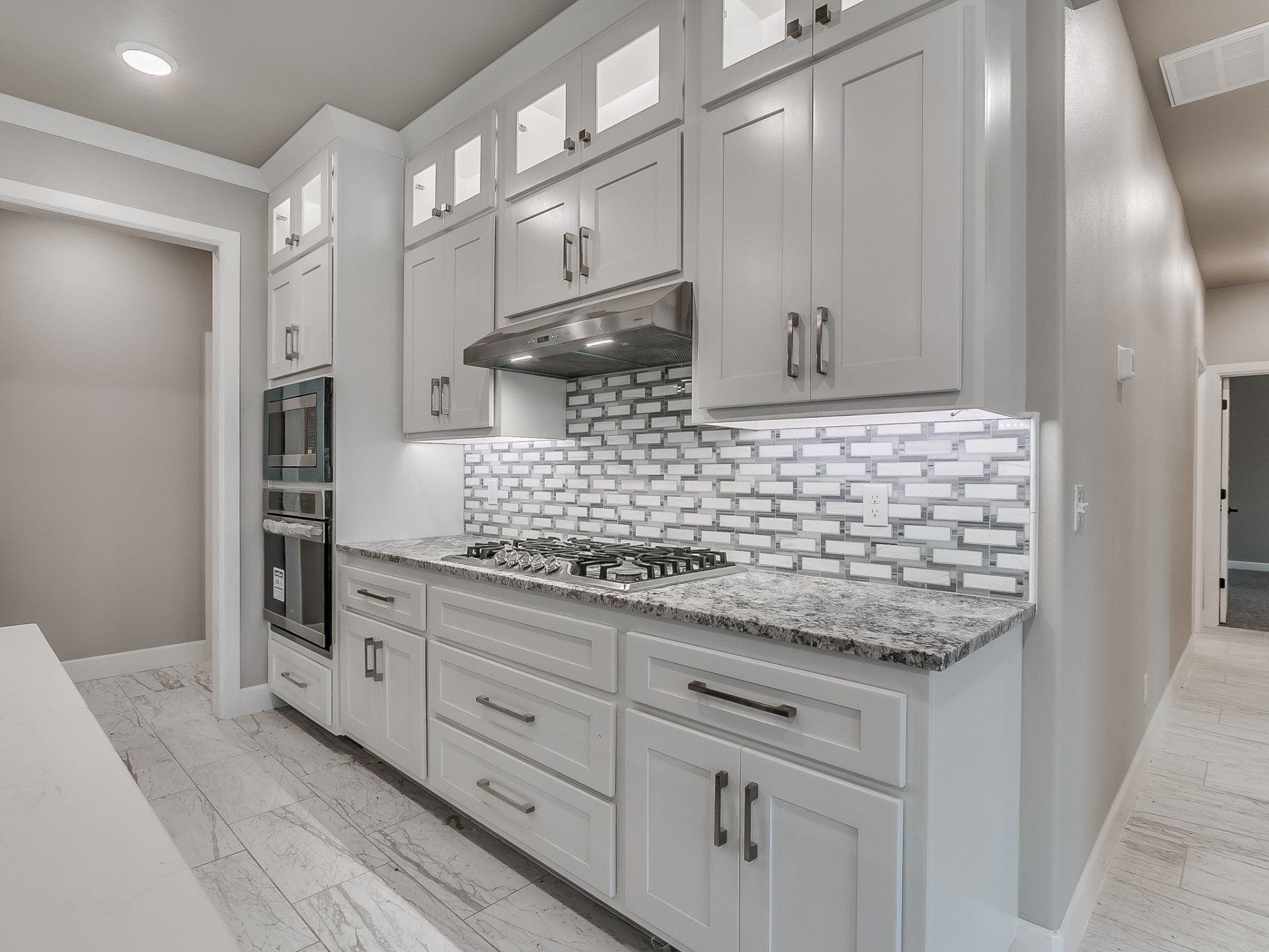 Modern kitchen featuring white cabinets, grey granite countertops, a brick-style backsplash, and stainless steel appliances.