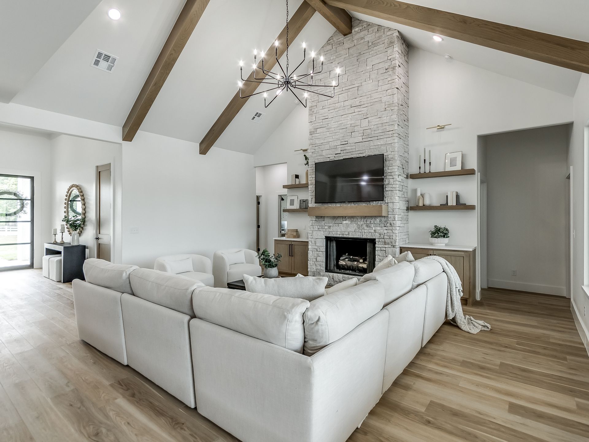 Modern living room with a white sectional sofa, vaulted ceiling with wood beams, brick fireplace, and chandelier.