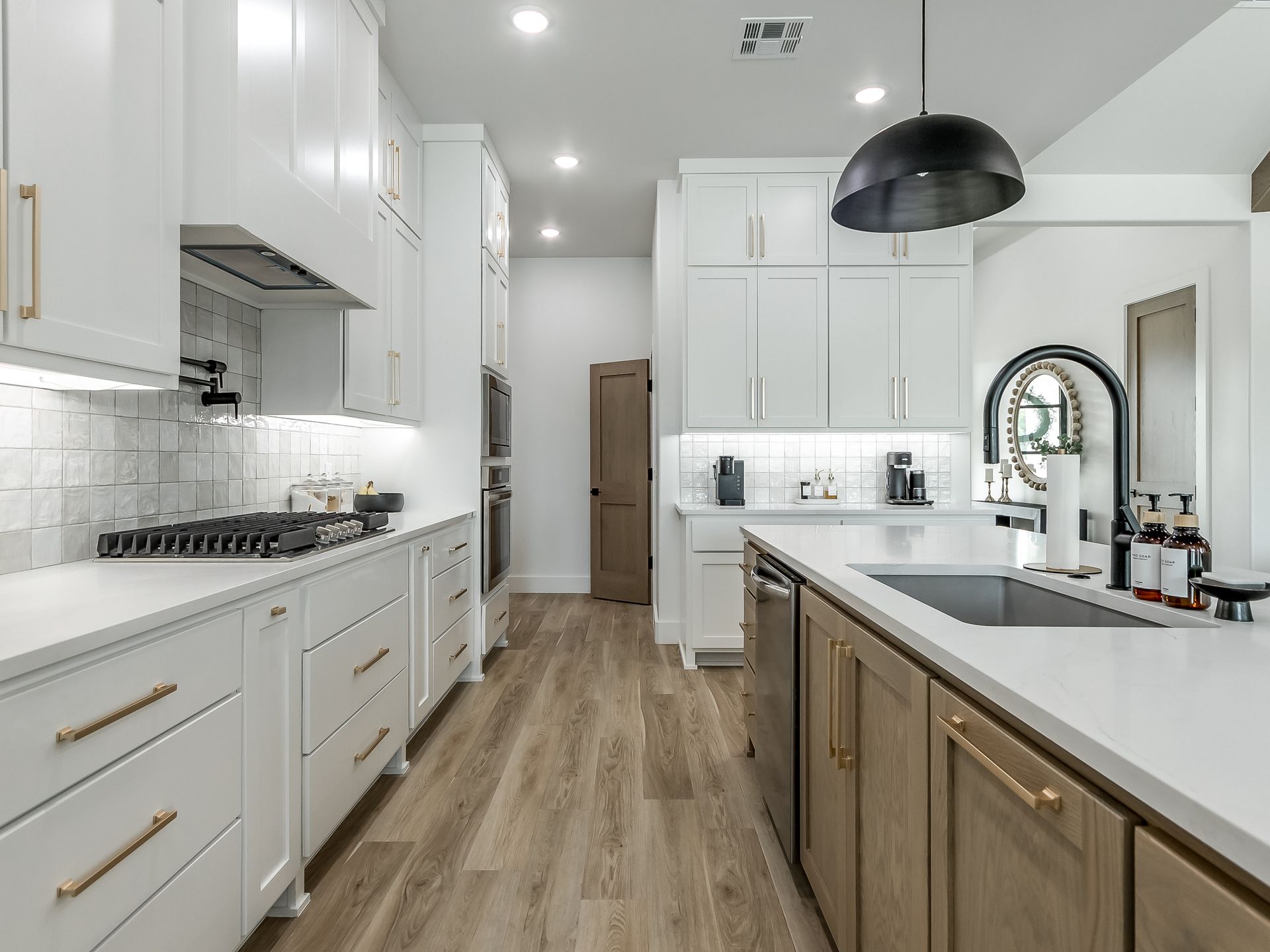 Modern kitchen with white upper cabinets, light wood base cabinets, white countertops, and a black pendant light.