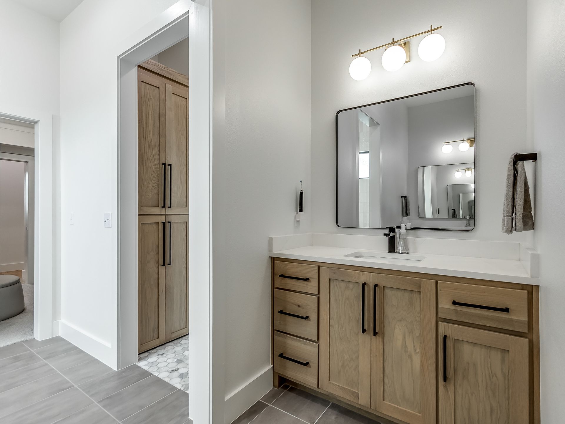 A modern bathroom vanity with a wood cabinet, white countertop, rectangular mirror, and gold light fixture.