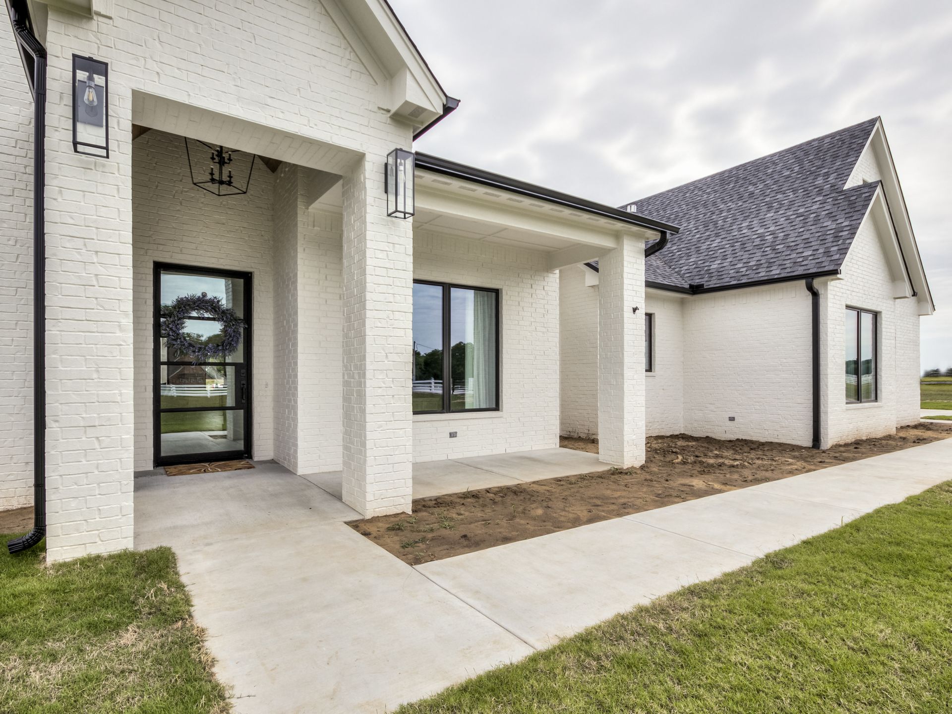 Exterior view of a modern white brick home with a covered front porch, dark-framed windows, and a black front door.