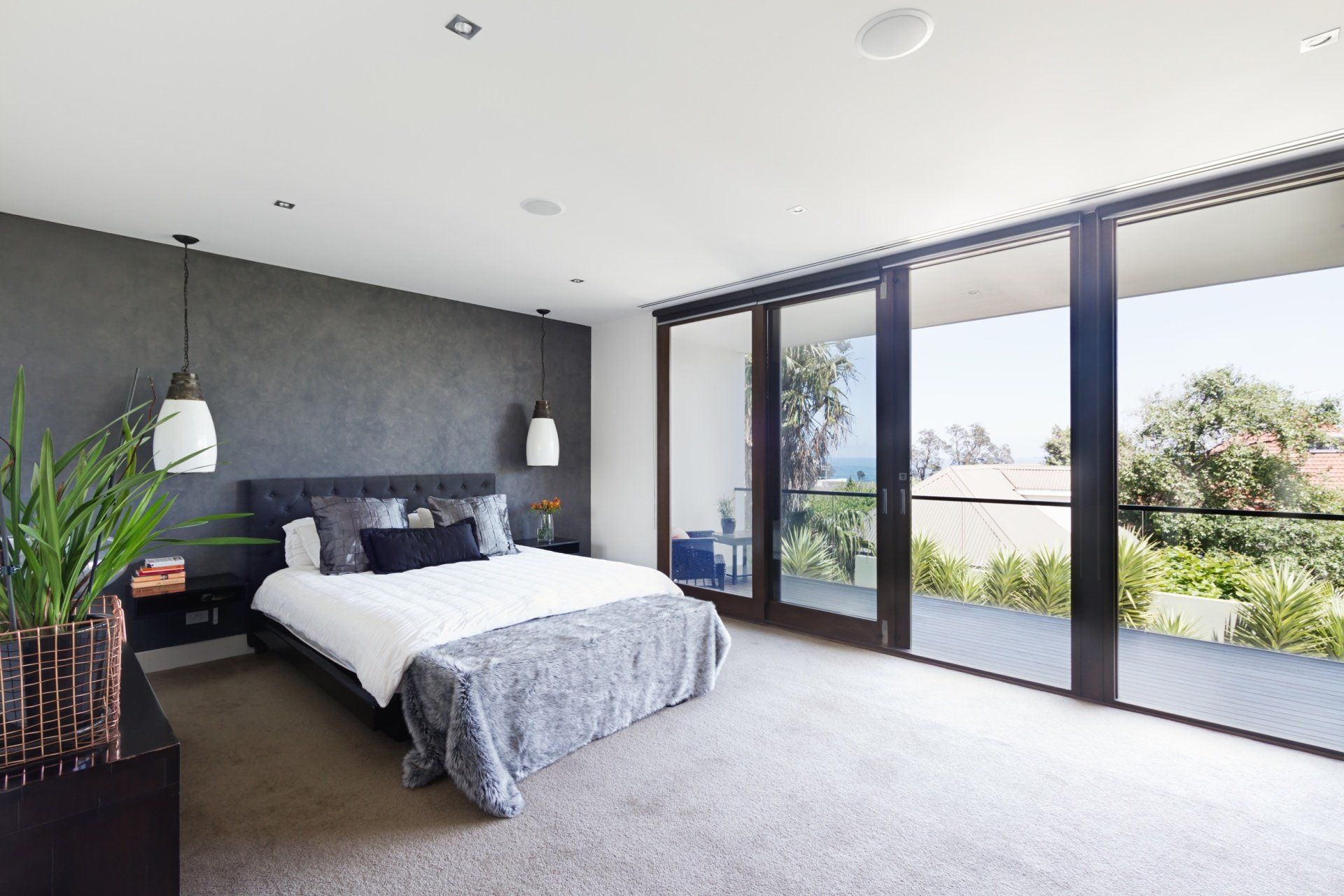 Modern bedroom with a gray accent wall, king bed, and floor-to-ceiling windows overlooking a lush outdoor terrace.