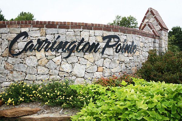 A stone entrance sign for Carrington Pointe, featuring black cursive lettering and landscaping in the foreground.