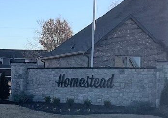 A stone wall entrance sign reads