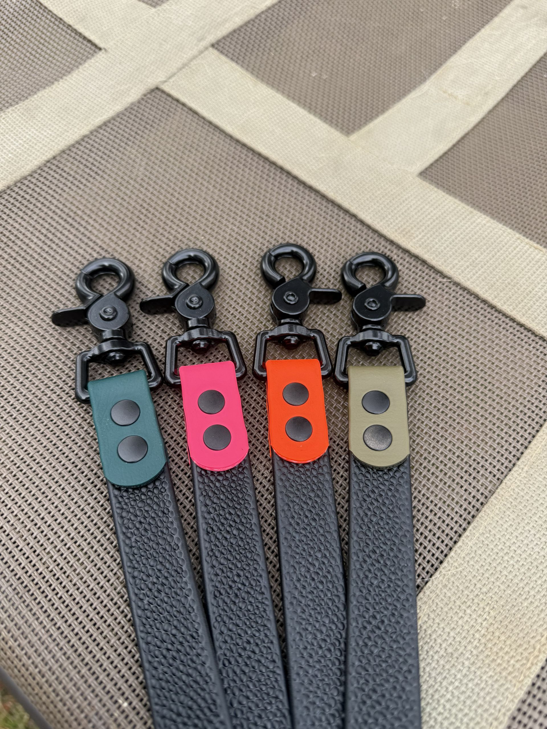 A black textured dog leash with a dark green connector and a black metal clasp, resting on a beige outdoor table.