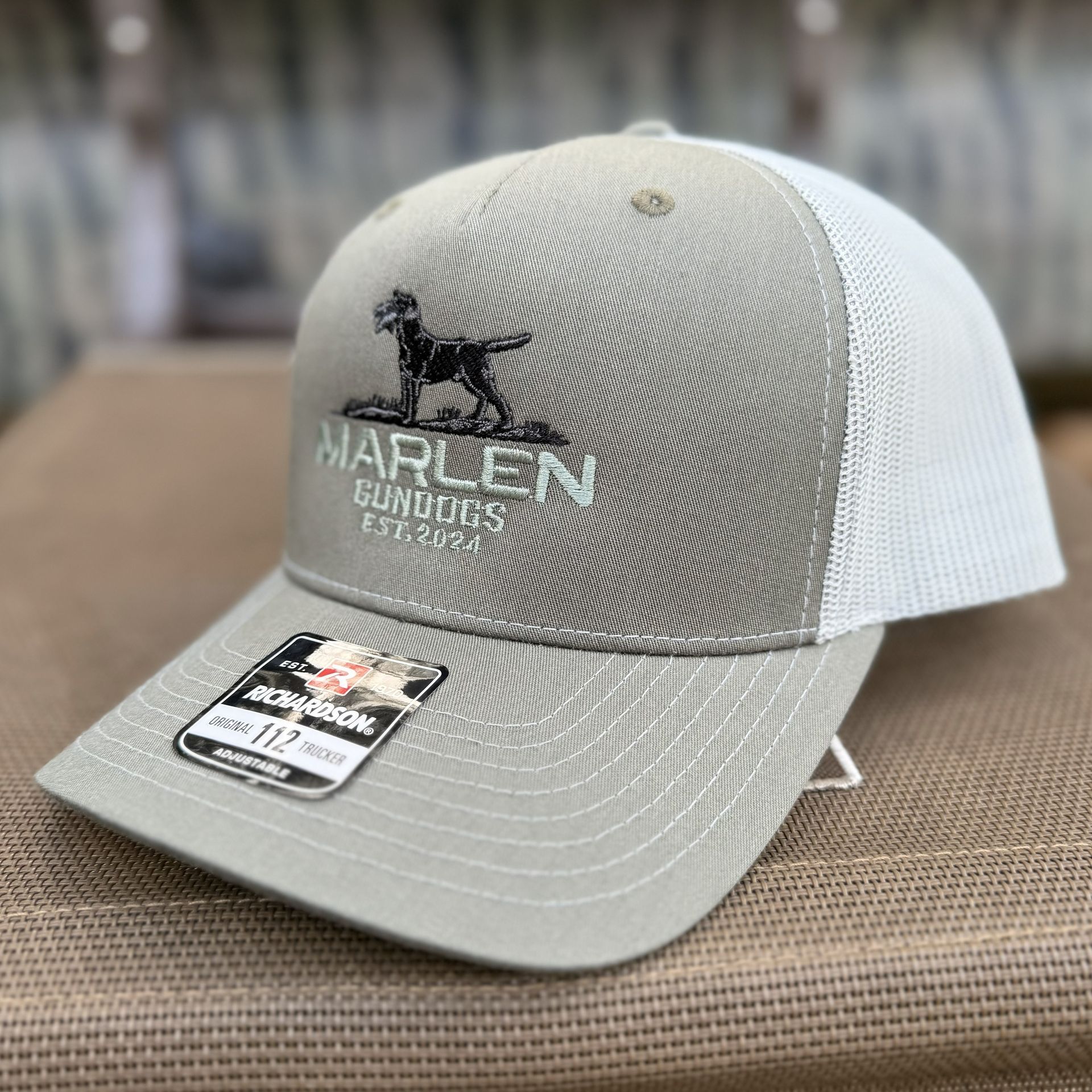 A tan and white trucker hat featuring an embroidered black dog logo and the text