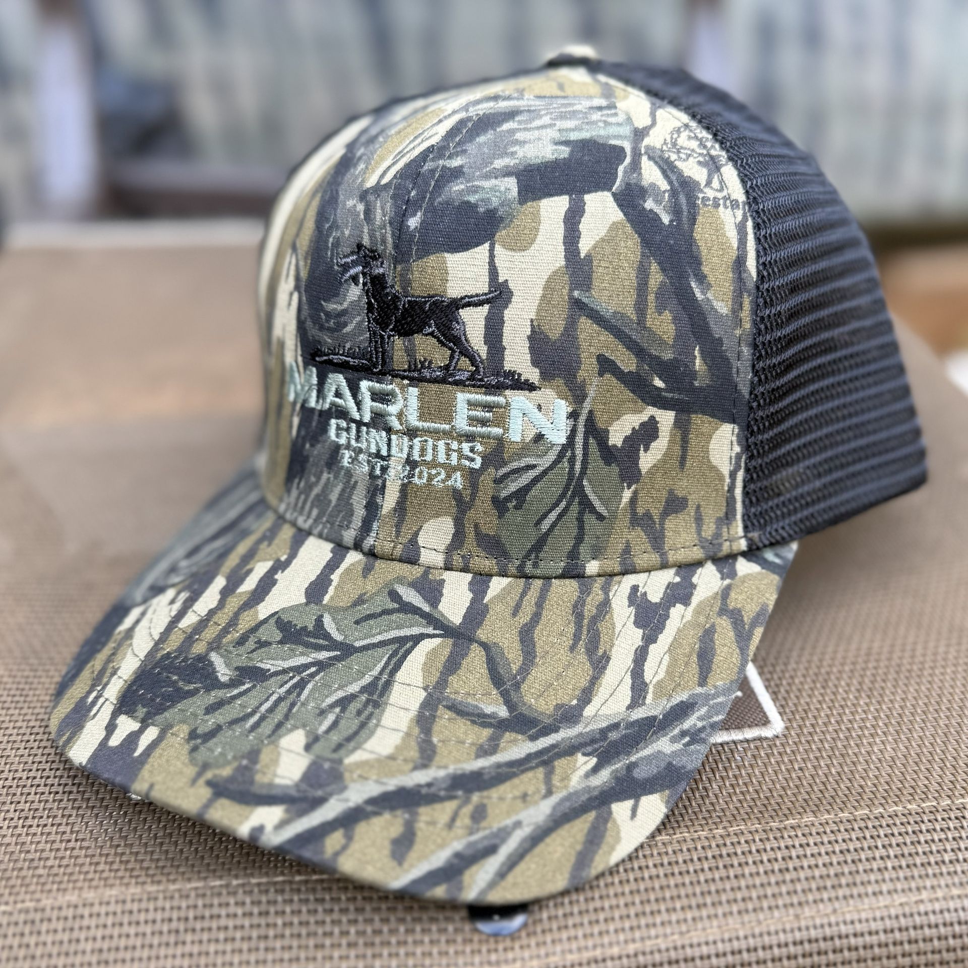 Camo trucker hat with a black mesh back and a logo featuring a dog silhouette and