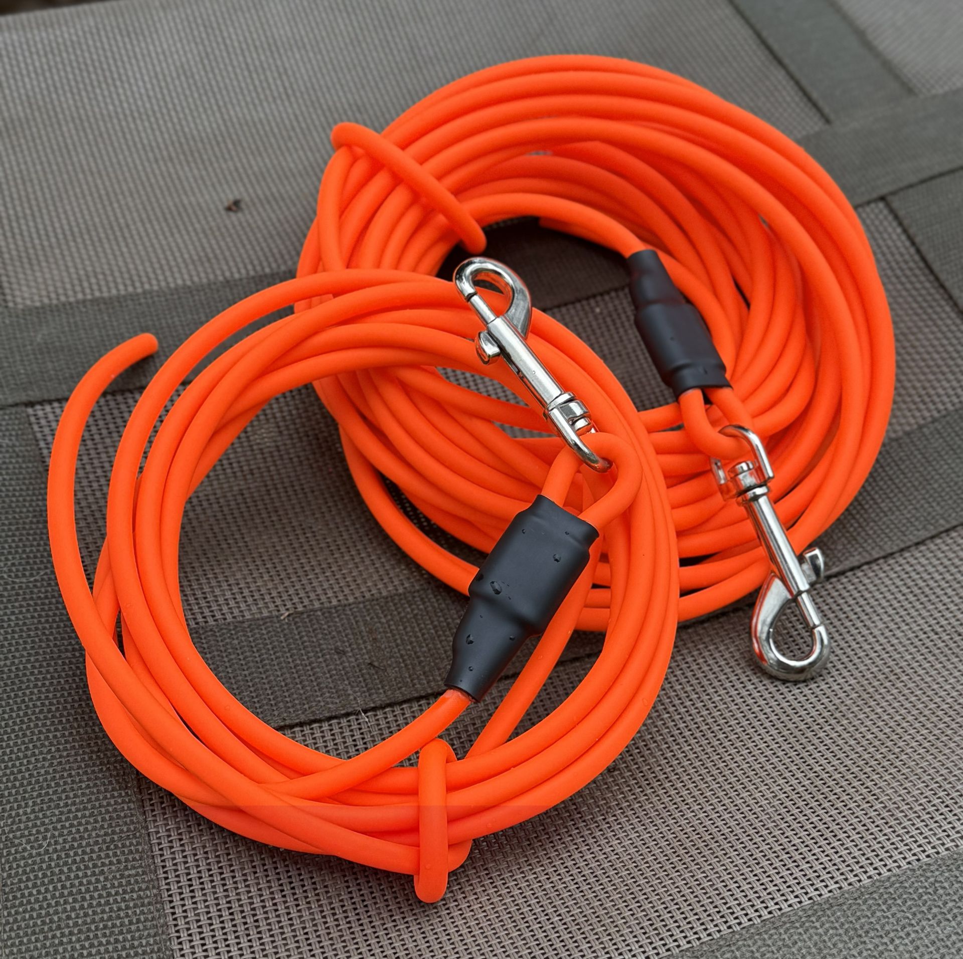 Two coiled bright orange leashes with silver metal clips, placed on a grey textured surface.
