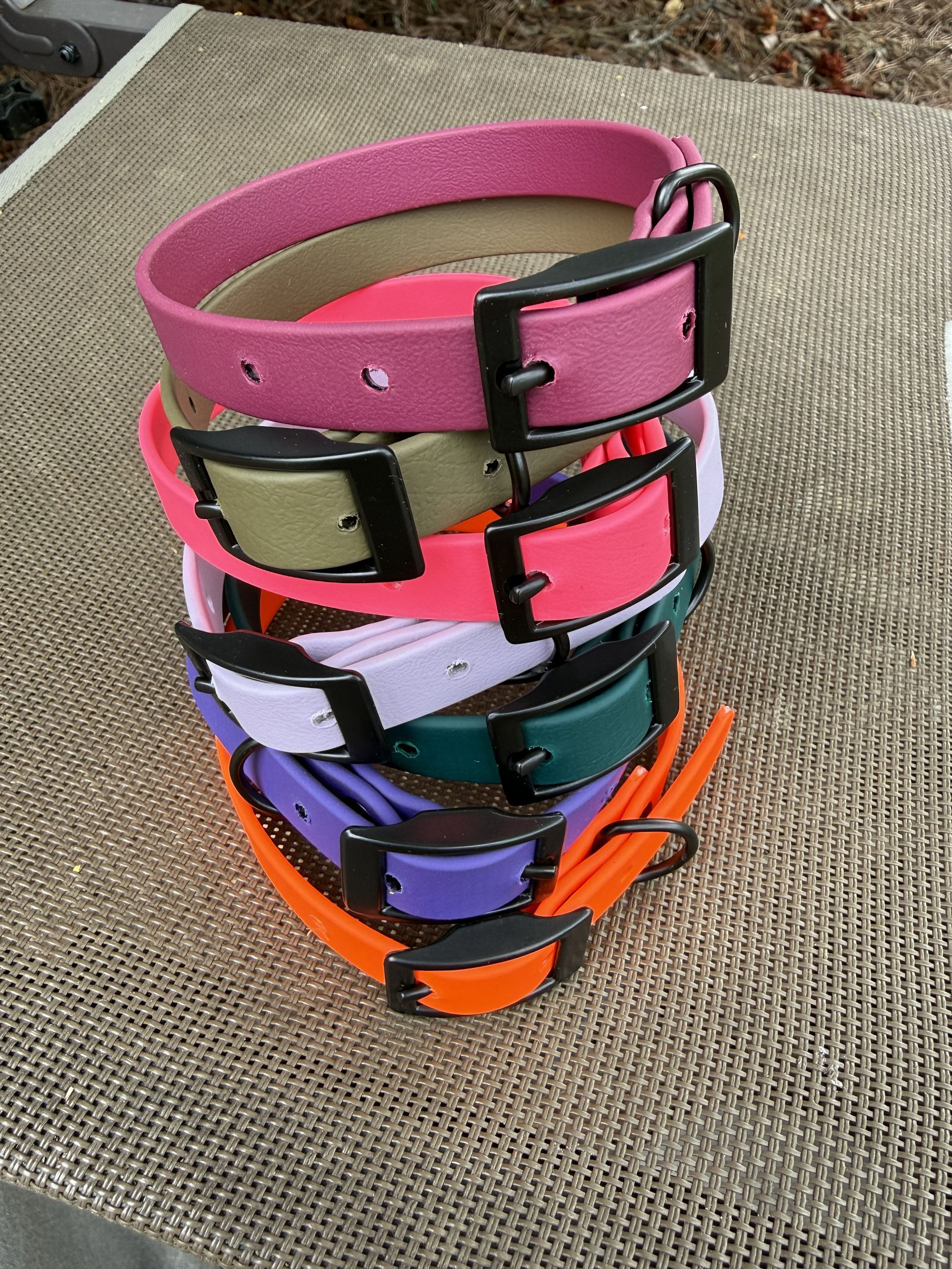 A vertical stack of brightly colored, flexible dog collars with black hardware, resting on a textured gray surface.