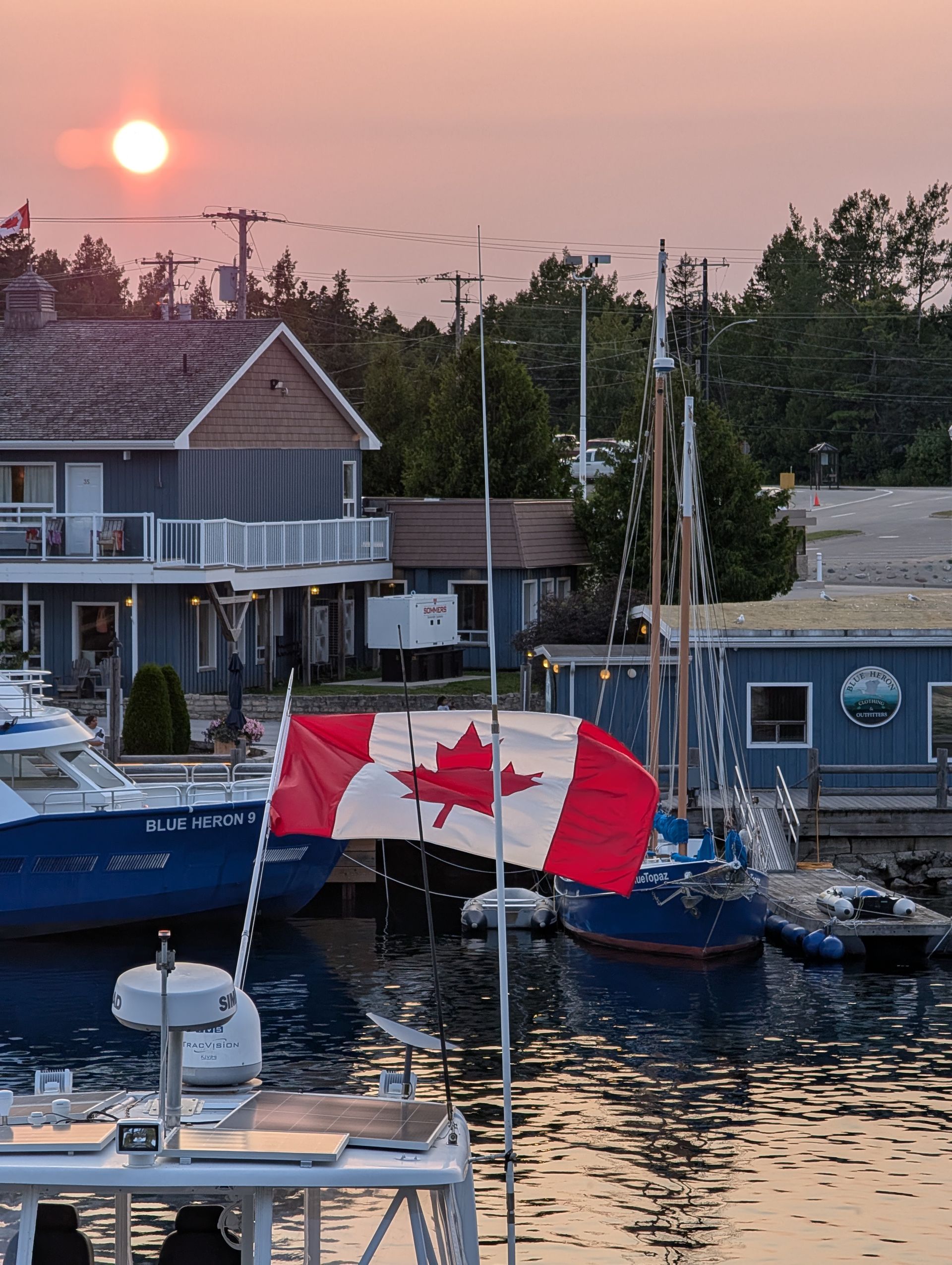 Canadian flag fluttering over a harbor at sunset, with boats and waterfront buildings in the background
