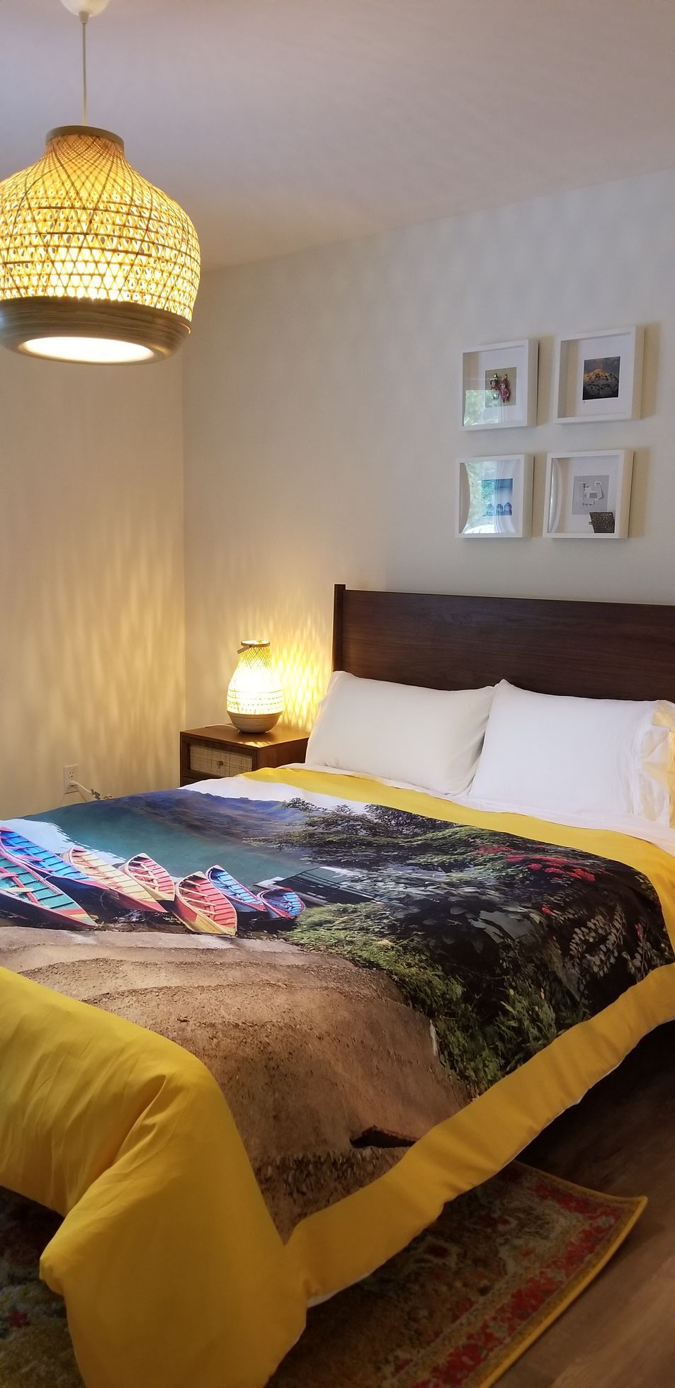 Cozy bedroom with a bed, bedside lamp, woven pendant light, and framed wall art.
