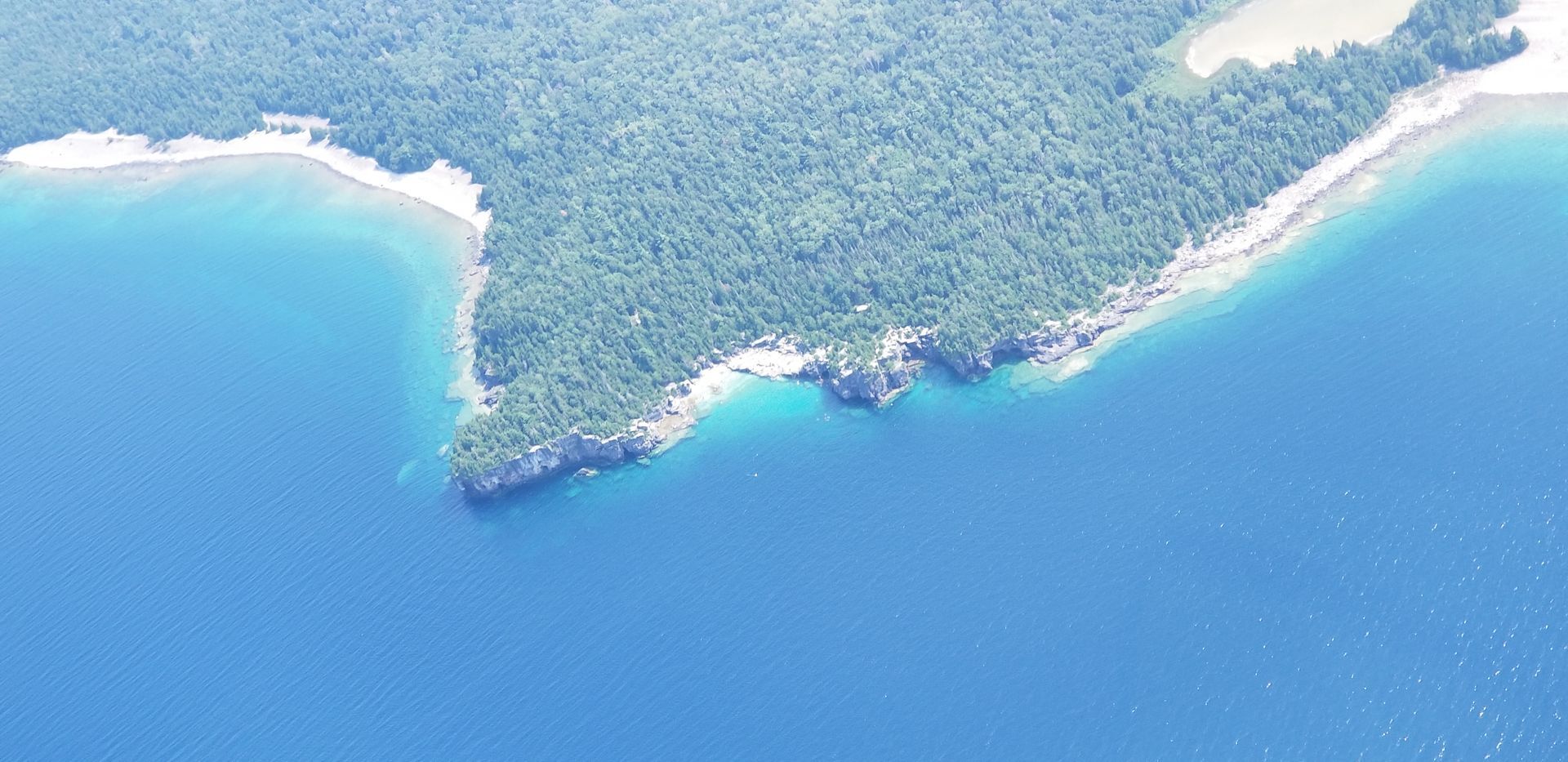 Aerial view of a tropical coastline with turquoise water, sandy shore, and dense green forest.