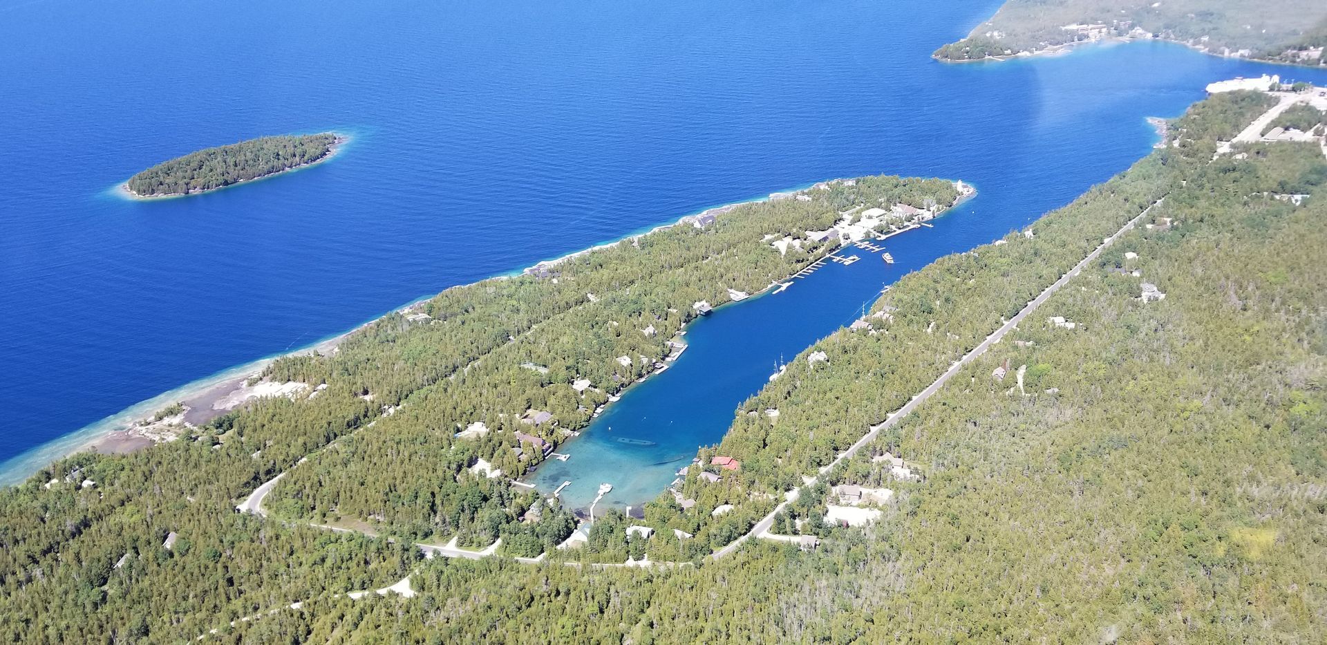 Aerial view of a narrow forested island with a blue lagoon and surrounding ocean, plus a small islet nearby