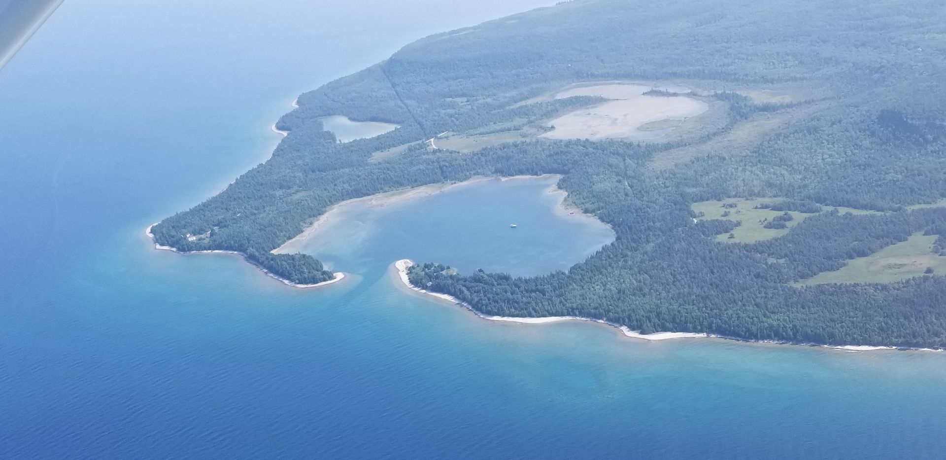 Aerial view of a green island with a crescent beach surrounded by blue ocean
