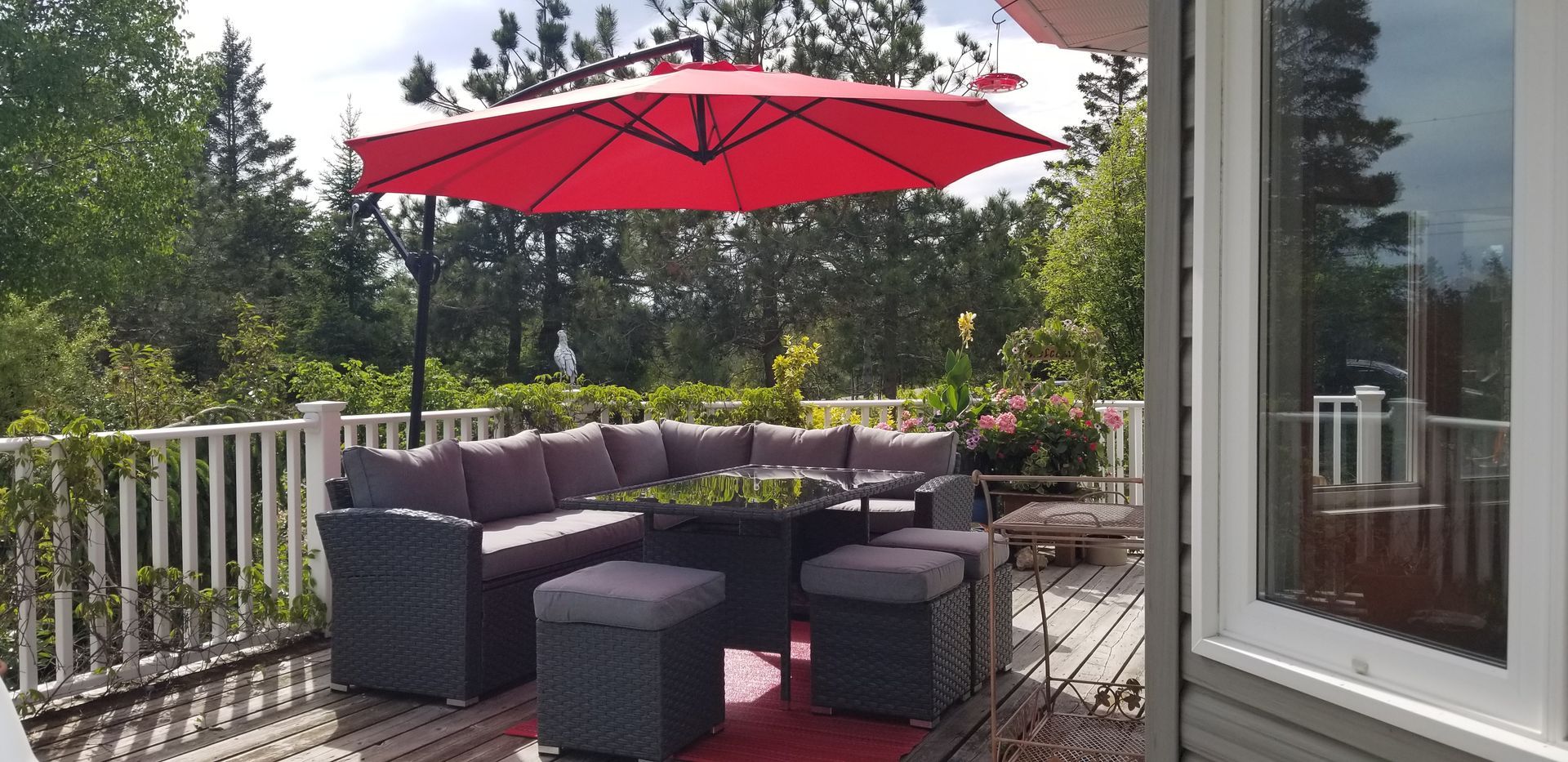 Outdoor patio with wicker seating, red umbrella, and a garden view