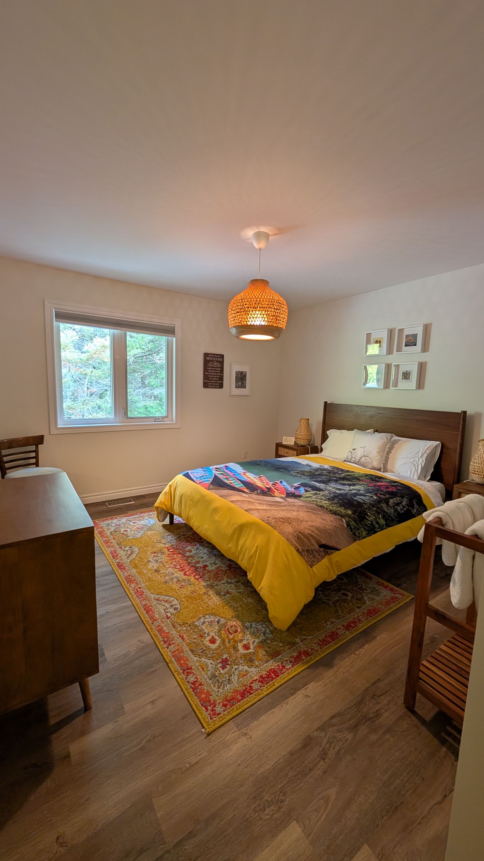 Cozy bedroom with a bed, patterned rug, window, and warm pendant light.
