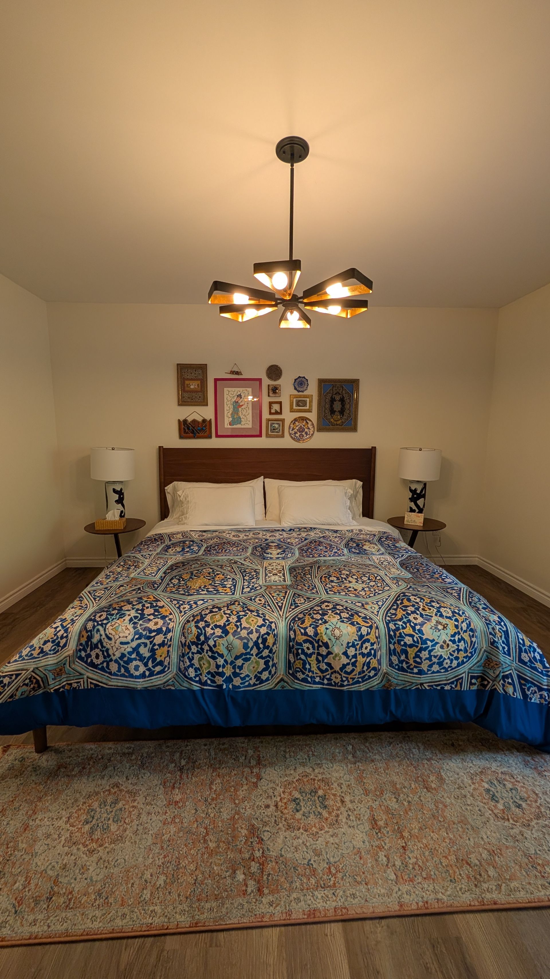 Cozy bedroom with a blue patterned bedspread, beige walls, chandelier, and framed art above the bed