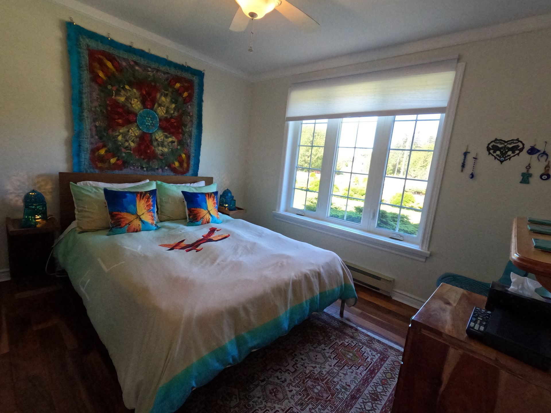 Cozy bedroom with a bed, colorful pillows, quilt, window, and tapestry on the wall.