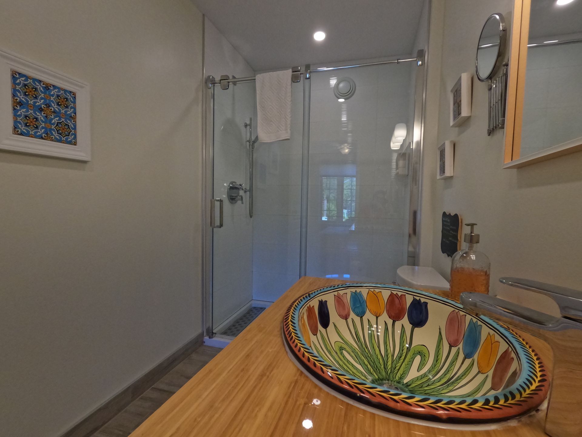 Modern bathroom with glass shower, colorful bowl sink, and wooden vanity