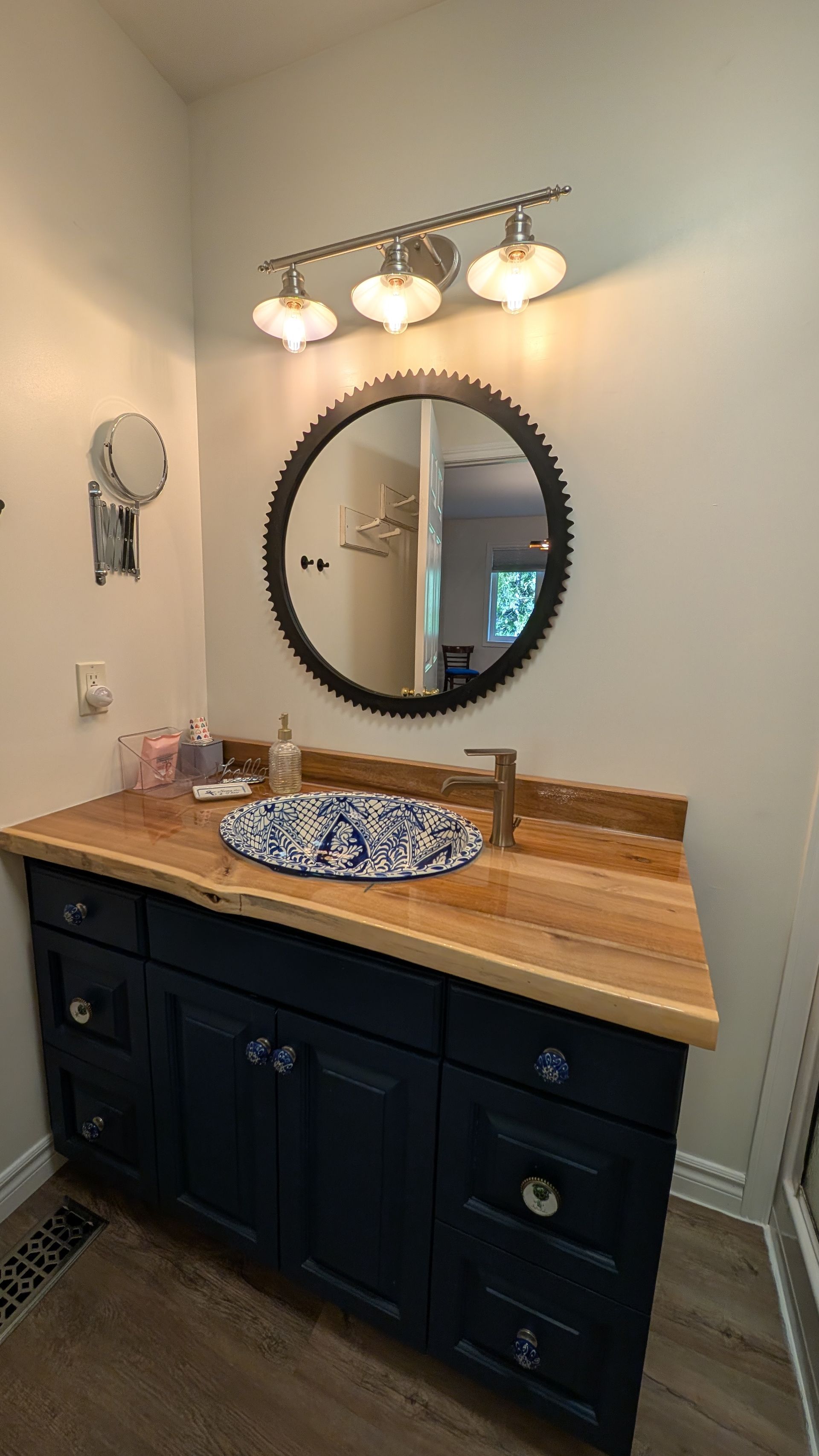 Bathroom vanity with dark cabinets, wood countertop, round mirror, and three-light fixture above.
