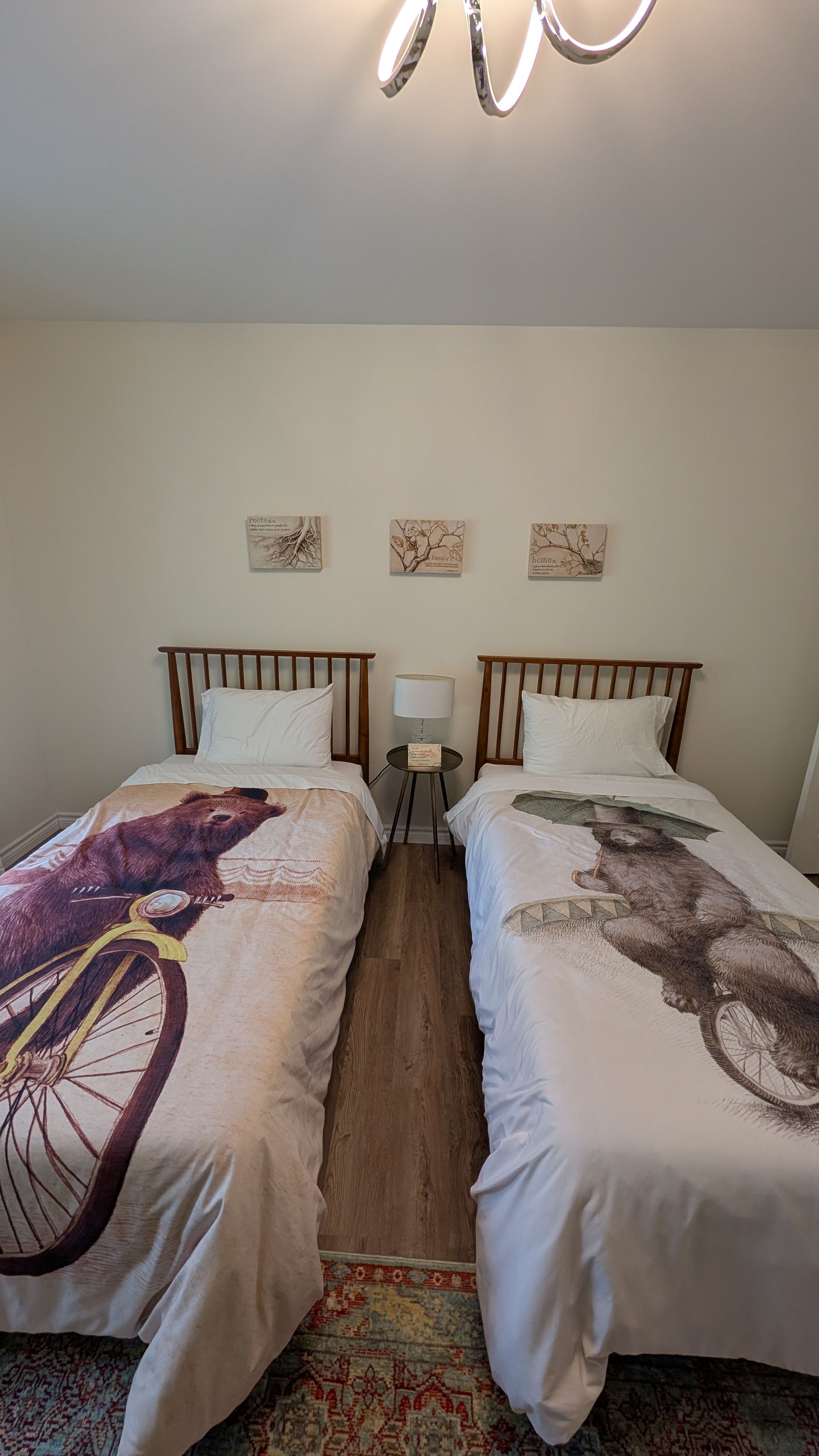 Two twin beds with patterned bedding in a cozy bedroom, with a nightstand and wall art between them.