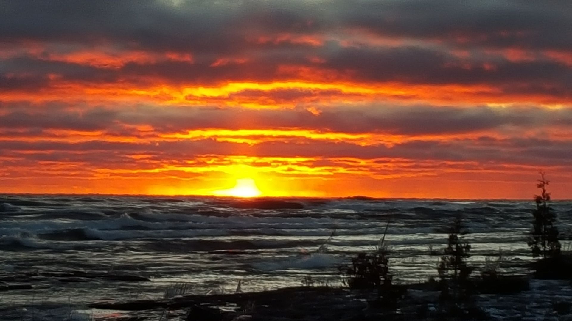 Sunset over a snowy shoreline with glowing orange clouds and dark water