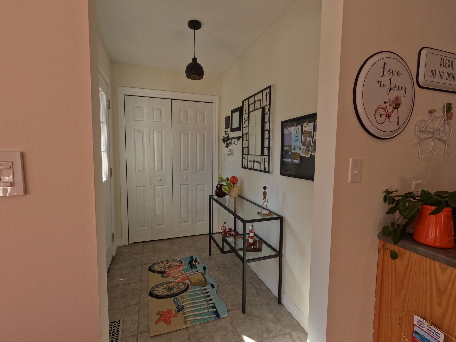 Hallway with white closet doors, a black console table, wall art, and a colorful rug leading to an entryway.