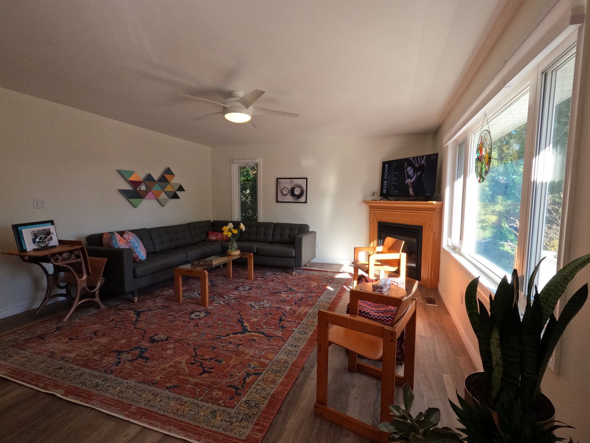 Bright living room with sectional sofa, patterned rug, fireplace, large windows, and potted plant