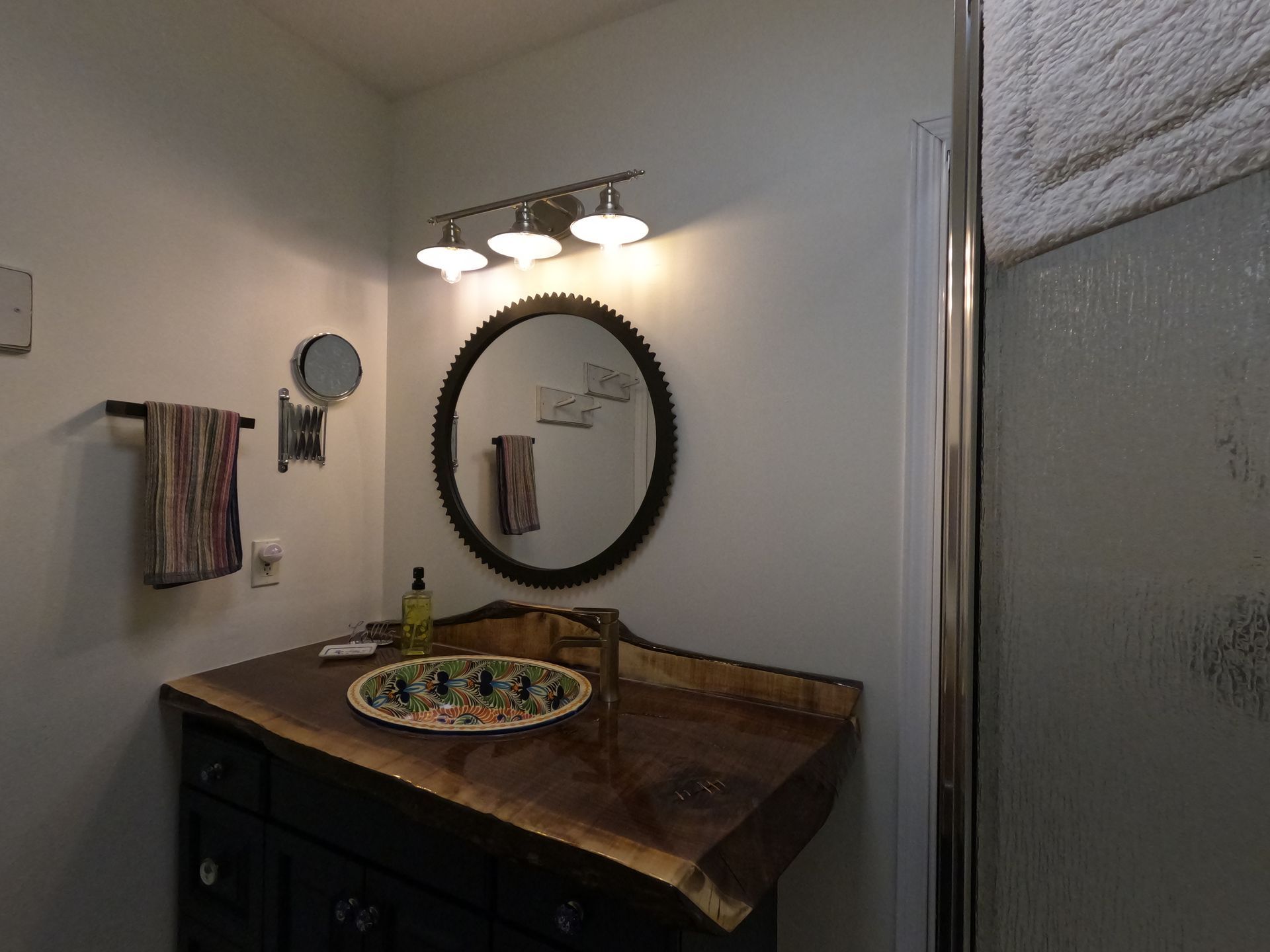 Small bathroom vanity with round mirror, three-light fixture, dark cabinet, and frosted window.