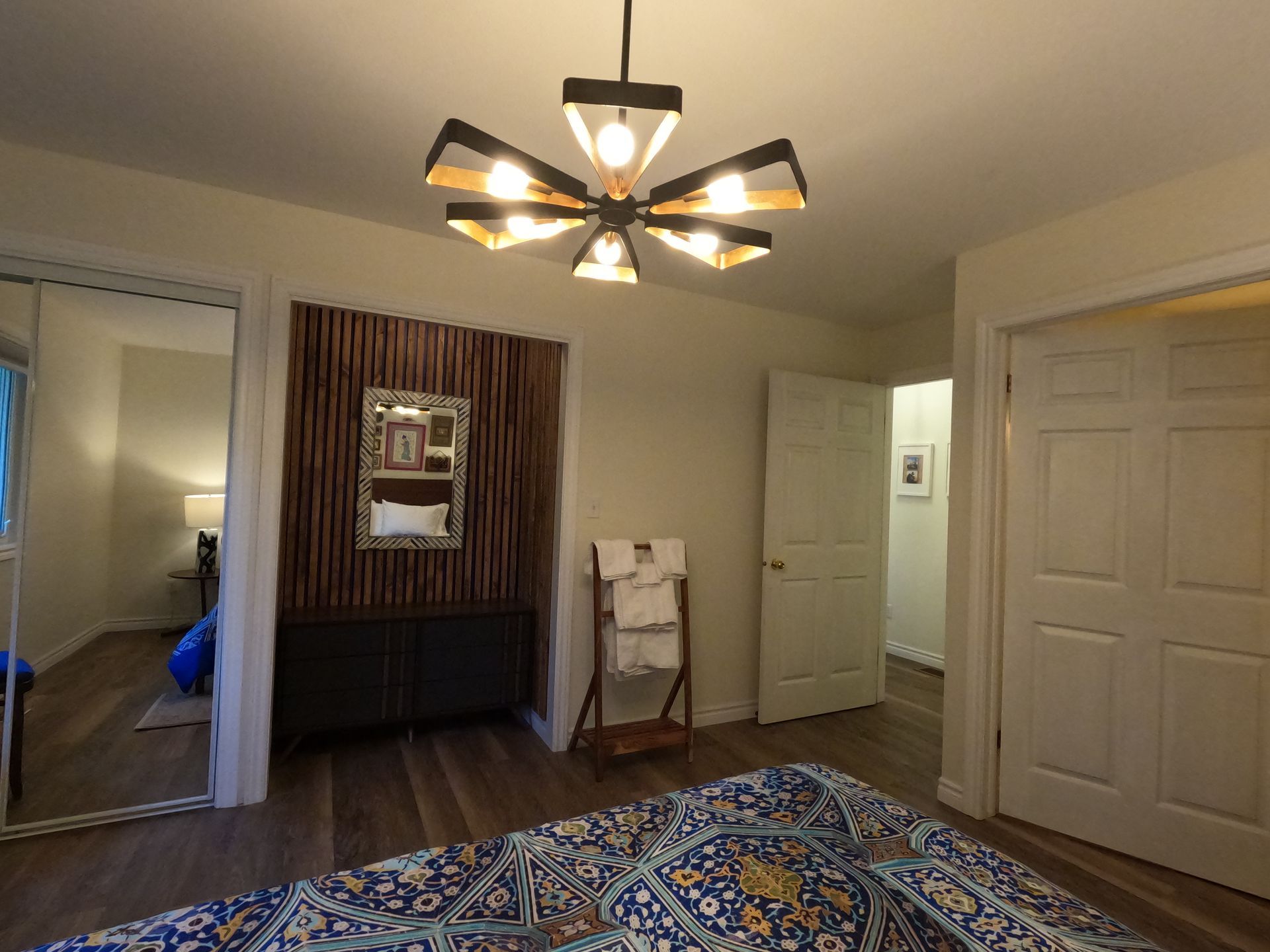 Modern bedroom with wood floor, ceiling fan light, mirrored closet doors, and a bed with colorful blanket