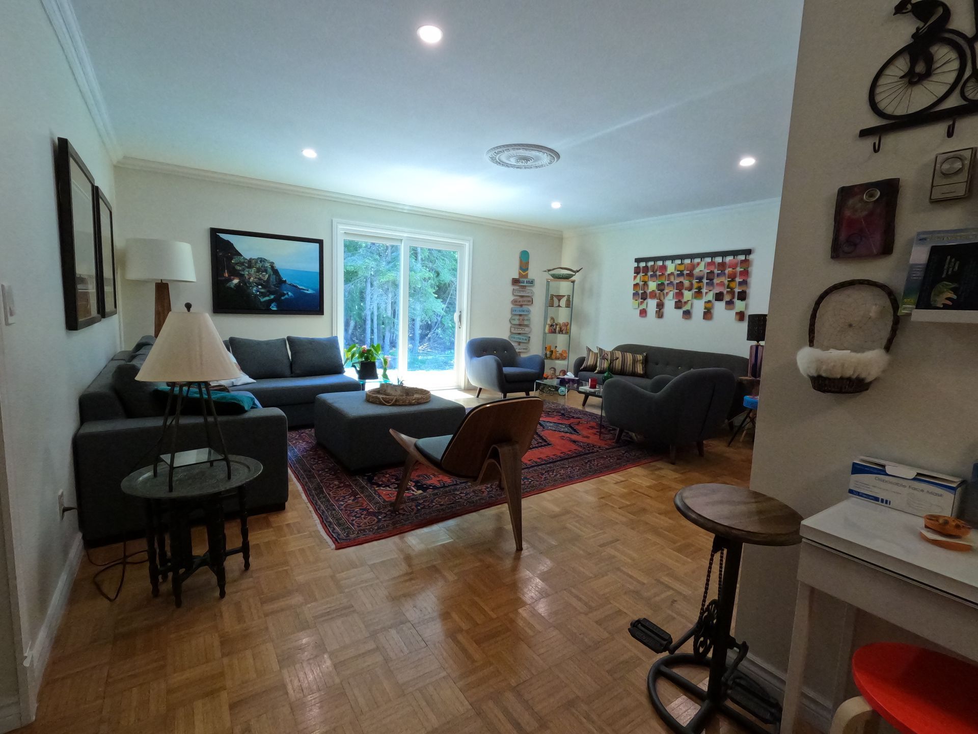 Bright living room with sectional sofas, coffee table, red rug, and large window overlooking greenery.