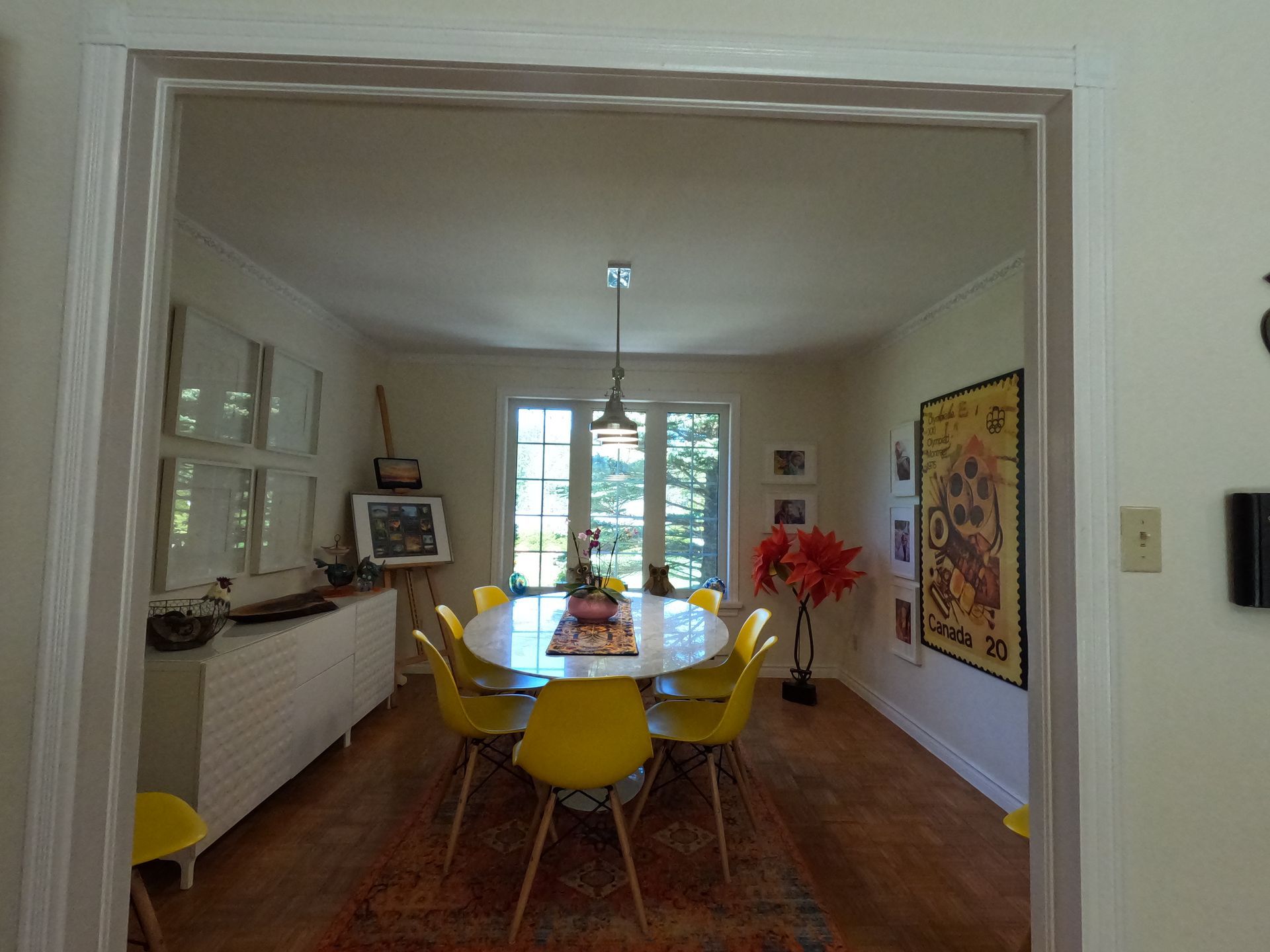 Dining room with yellow chairs, round table, red rug, and a large window at the far end