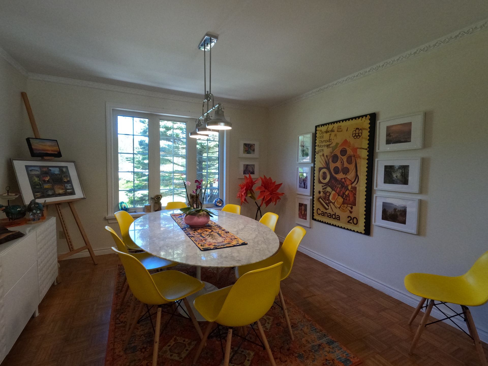 Bright dining room with yellow chairs, oval table, artwork, and sunlight from a window
