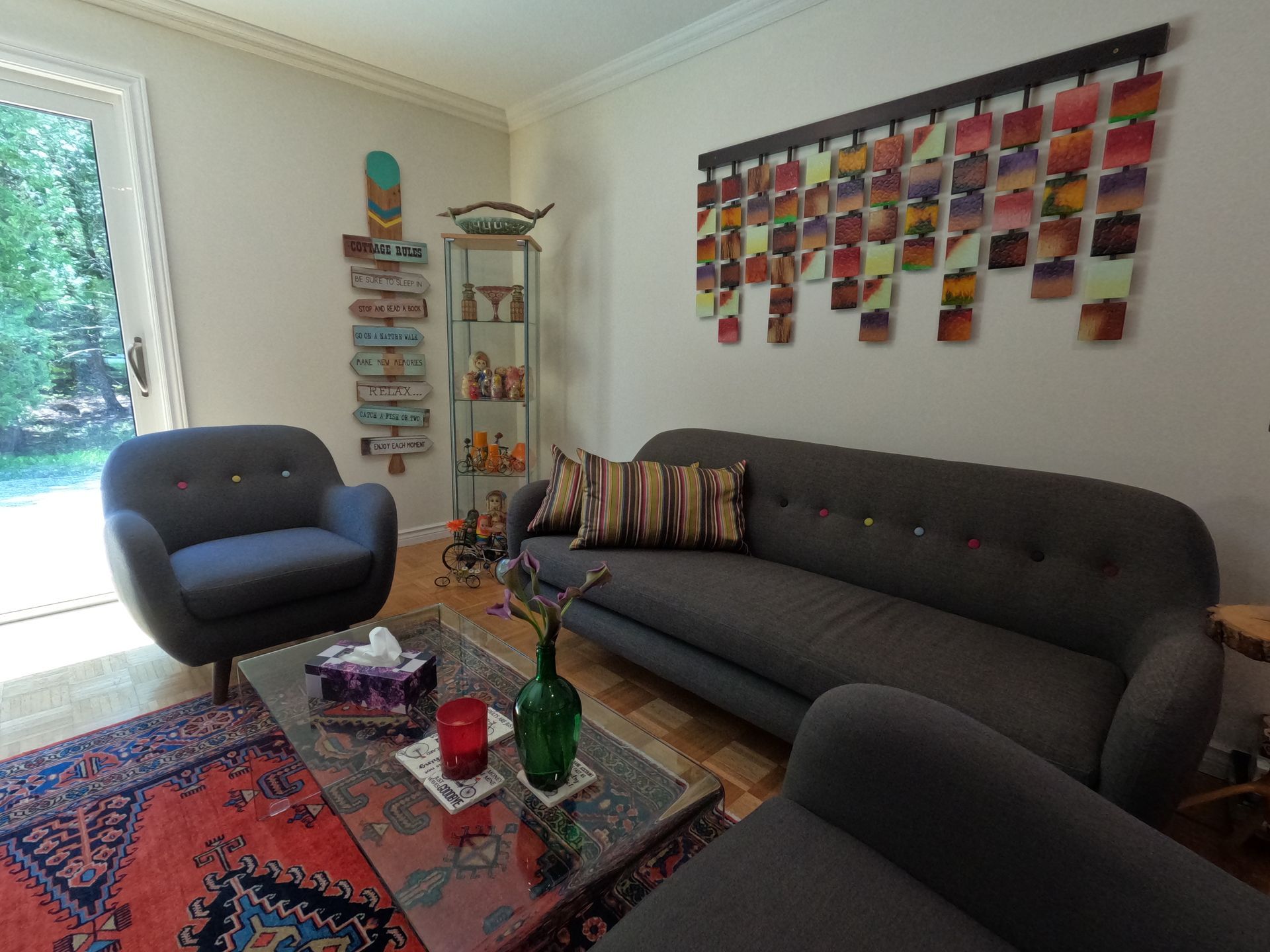 Modern living room with gray sofa, black chair, glass coffee table, and colorful wall art near a window