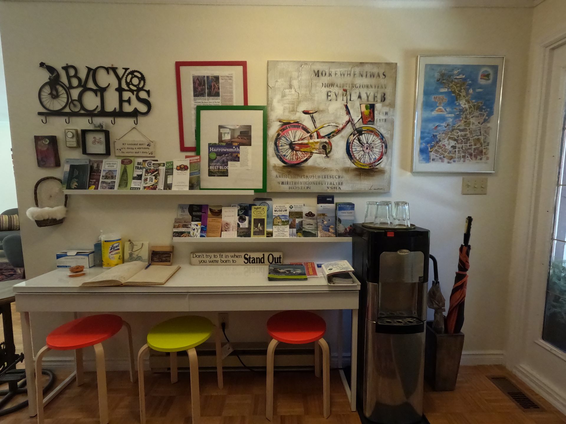 Home office corner with white desk, colorful stools, wall art, and a bicycle-themed display.